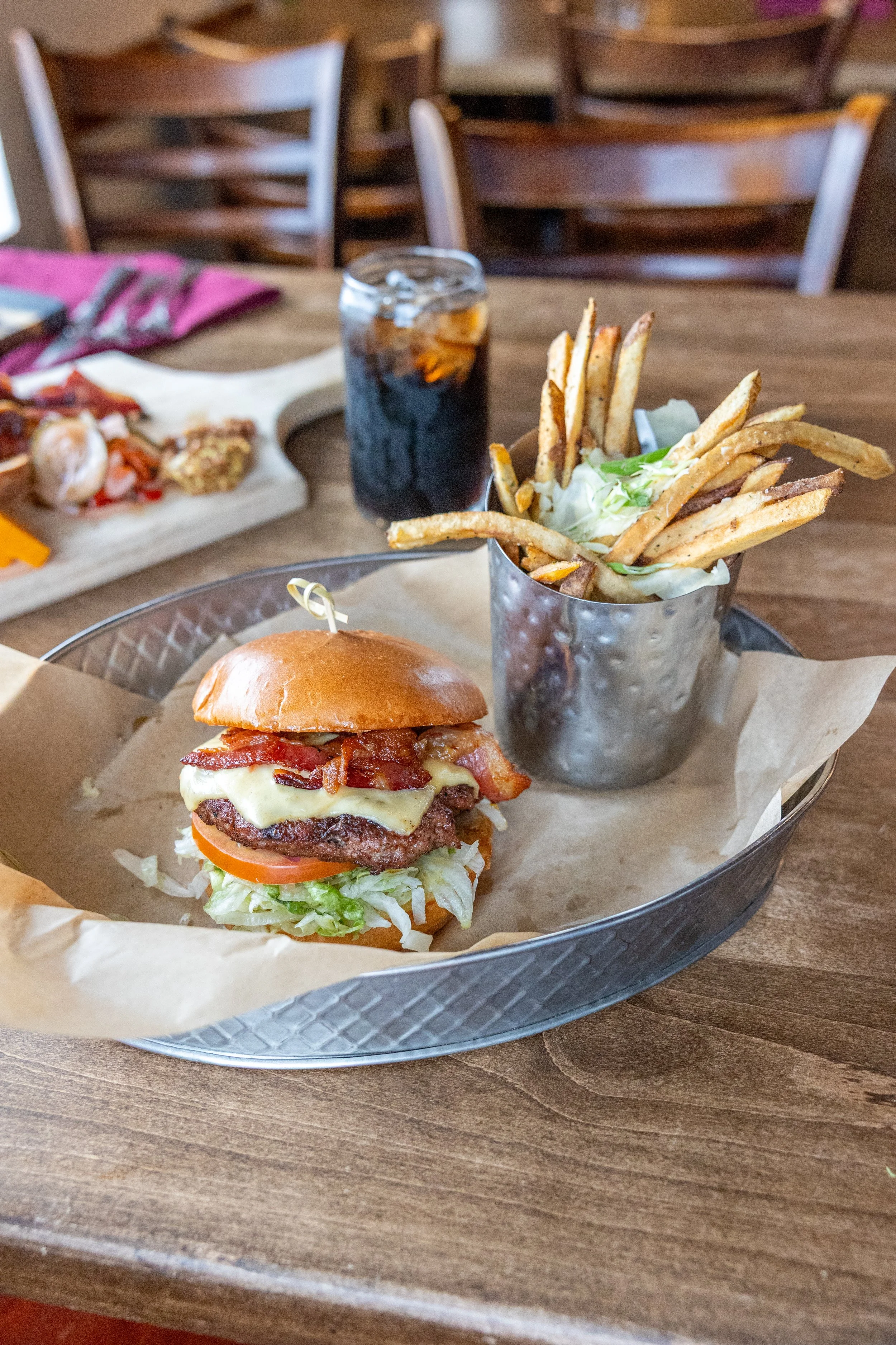 A meal on a metal tray featuring a fried egg on a sandwich bun, a small cup of ketchup, a metal cup of chopped cooked meat with shredded cheese and garnish, a glass of beer, a basket of fried chicken, and a salad in the background.