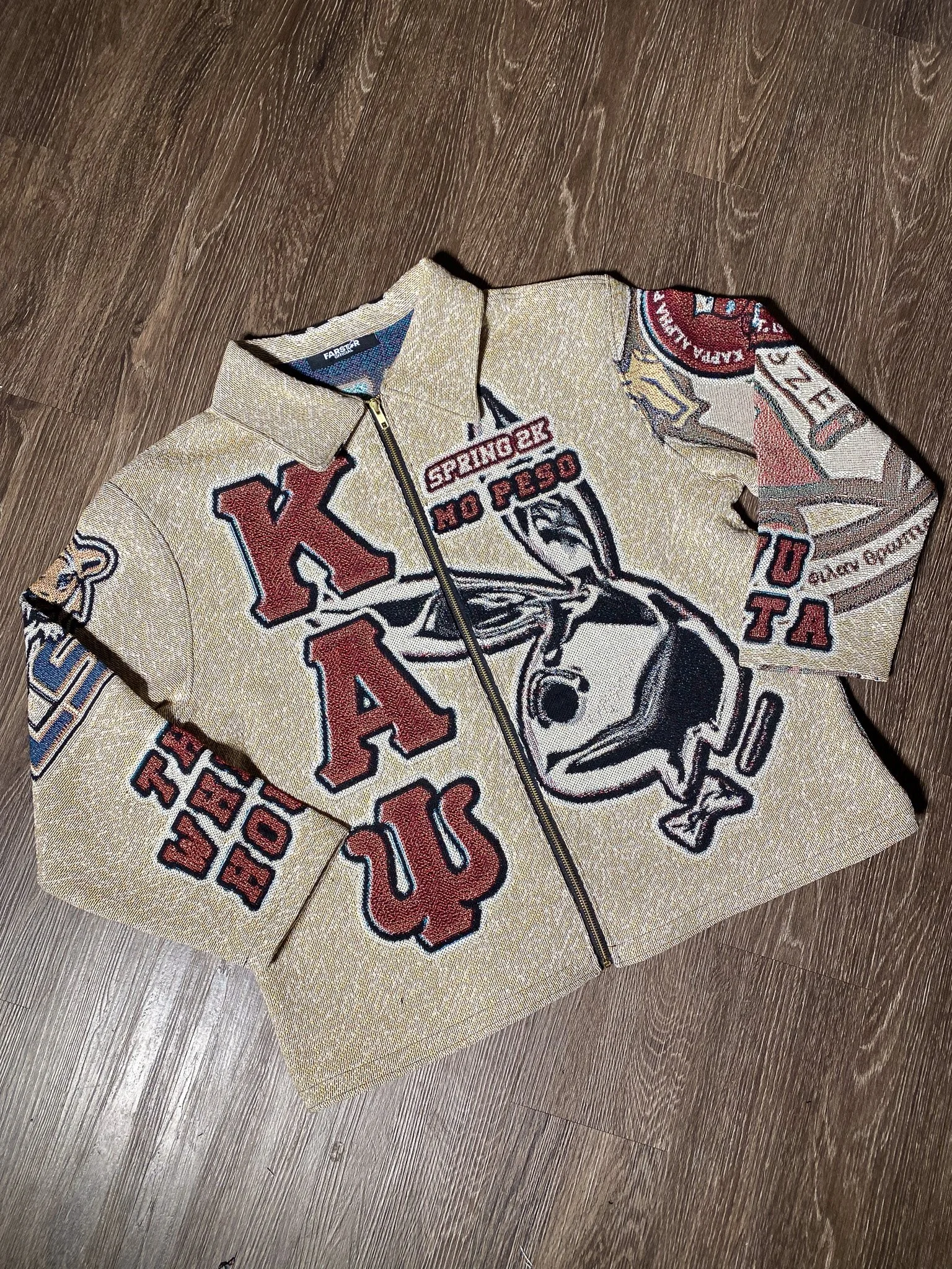 A vintage-style jacket with red, black, and white patches and embroidered text, lying on a wooden floor.
