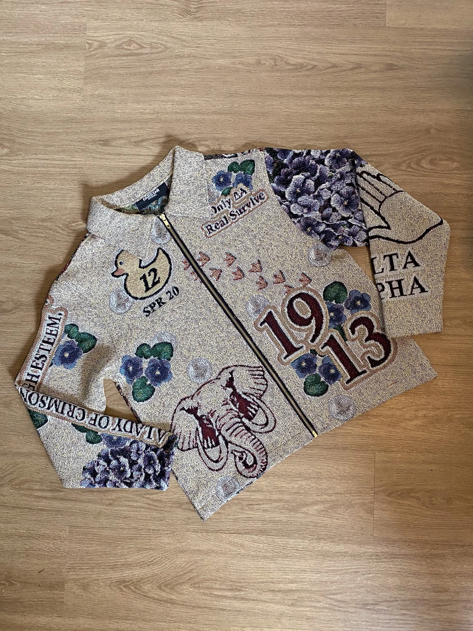 Close-up of a vintage embroidered racing jacket with floral and textual designs, lying on a wooden surface.