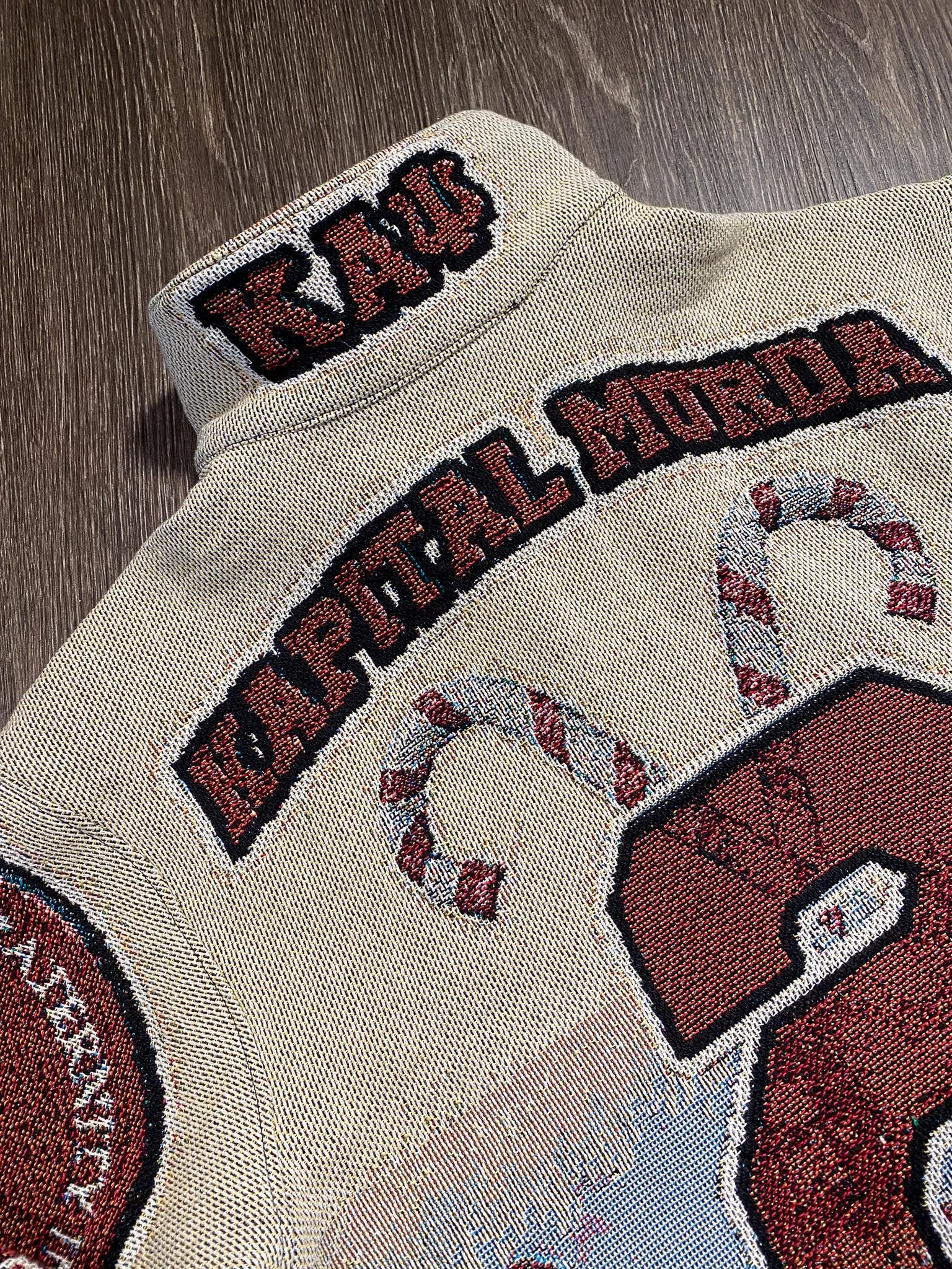 Close-up of a fabric patch with embroidered text and design, featuring red and black thread on a beige background.