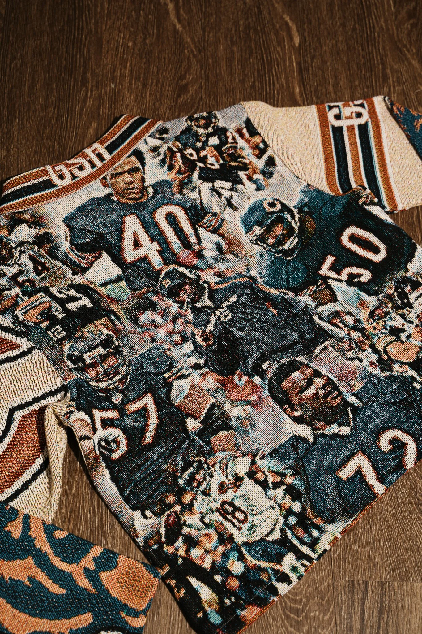 Close-up of a tapestry or woven fabric with sports figures, numbers, and intricate designs, laid on a wooden surface.