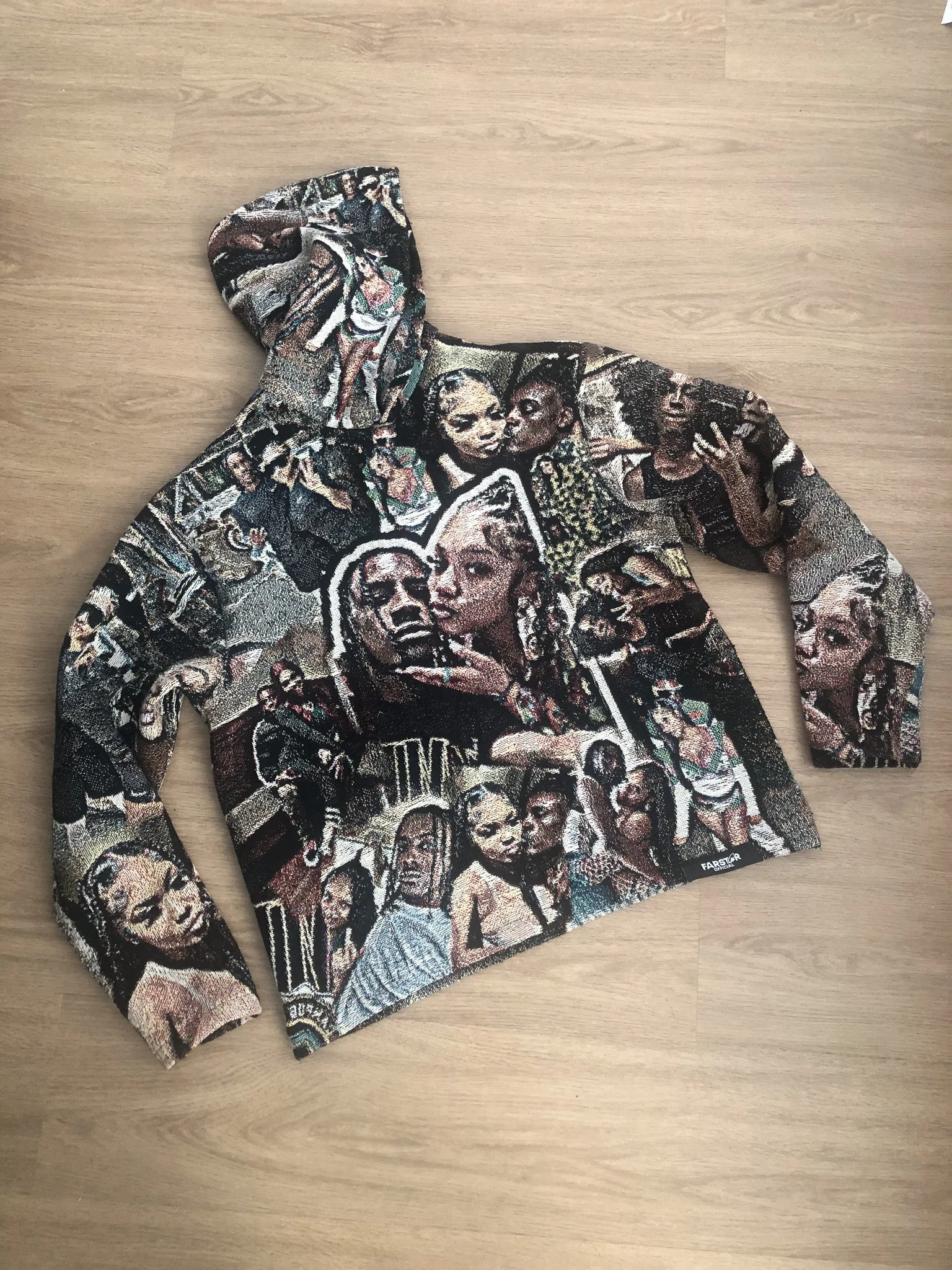 A colorful hoodie with a collage of various images of Black women on the fabric, laid flat on a wooden surface.