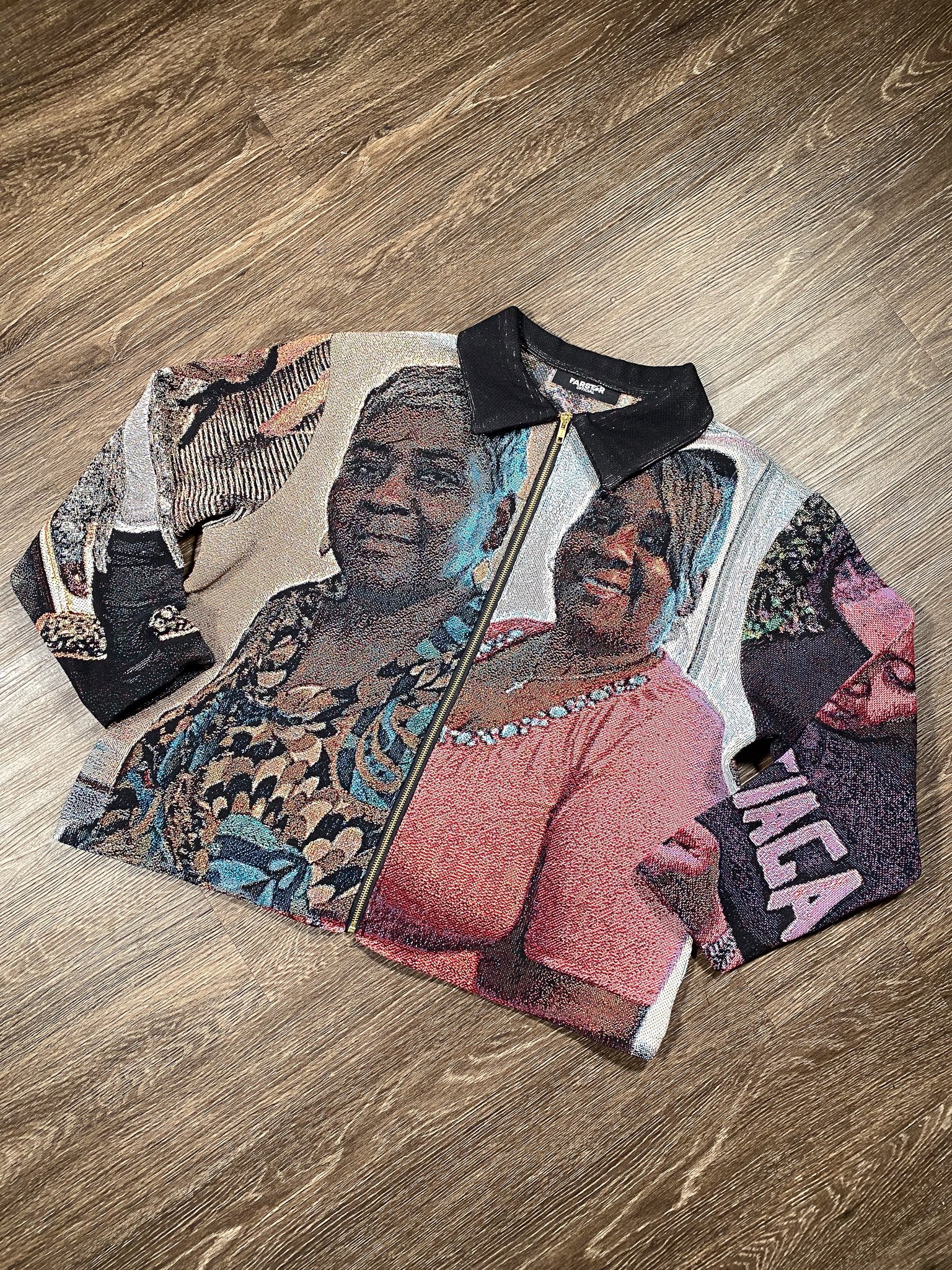 A jacket with a detailed image of two women, one with glasses and jewelry, and the word "FEAR" printed on the sleeve, lying on a wooden floor.