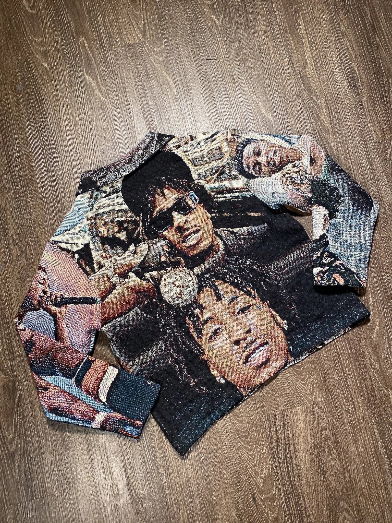 A long-sleeve shirt with a printed design of hip-hop artists, including Tupac Shakur, on a wooden floor.