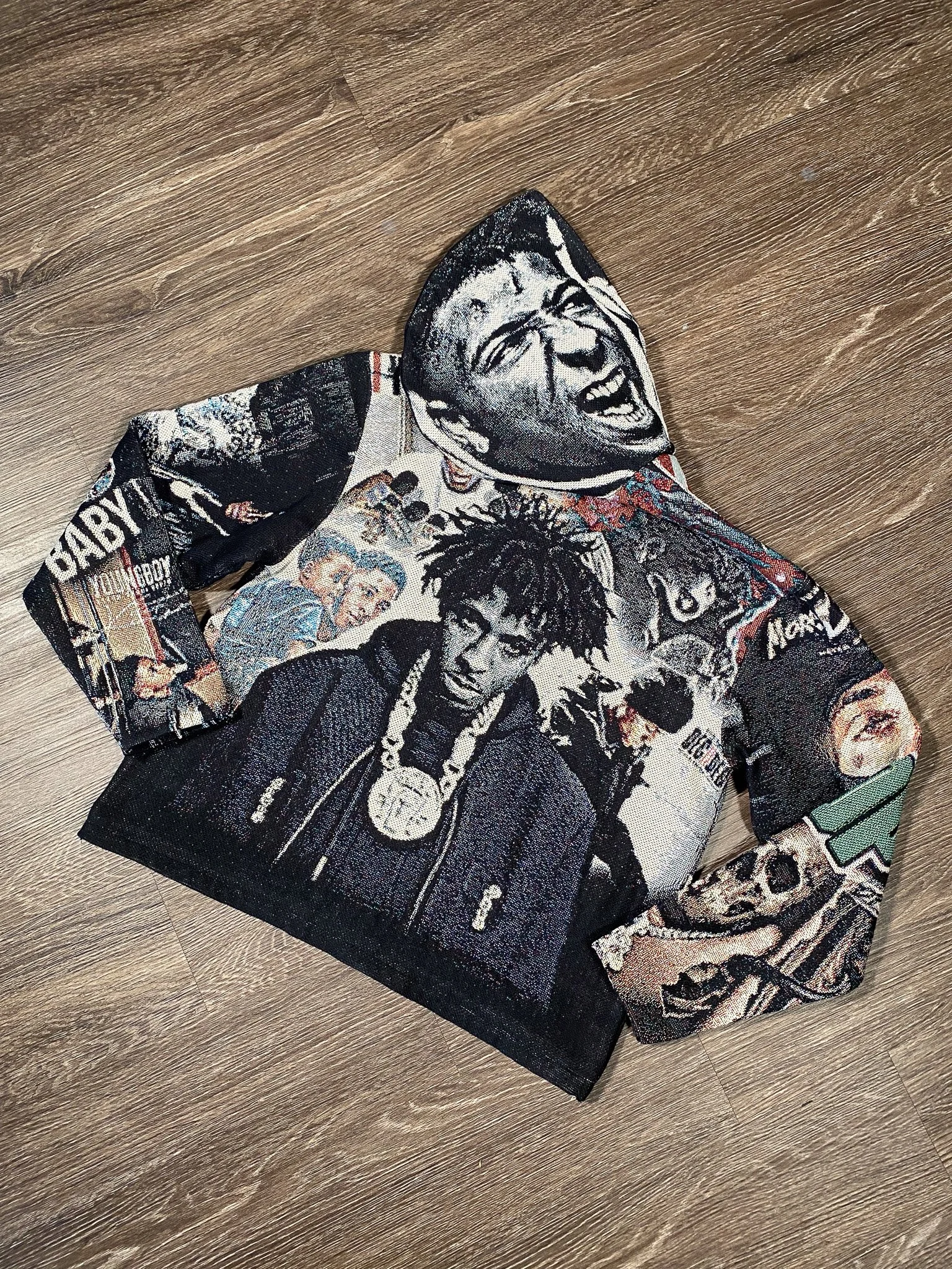 A sweater featuring a collage of images of rapper Tupac Shakur and other pop culture references, laid flat on a wooden surface.