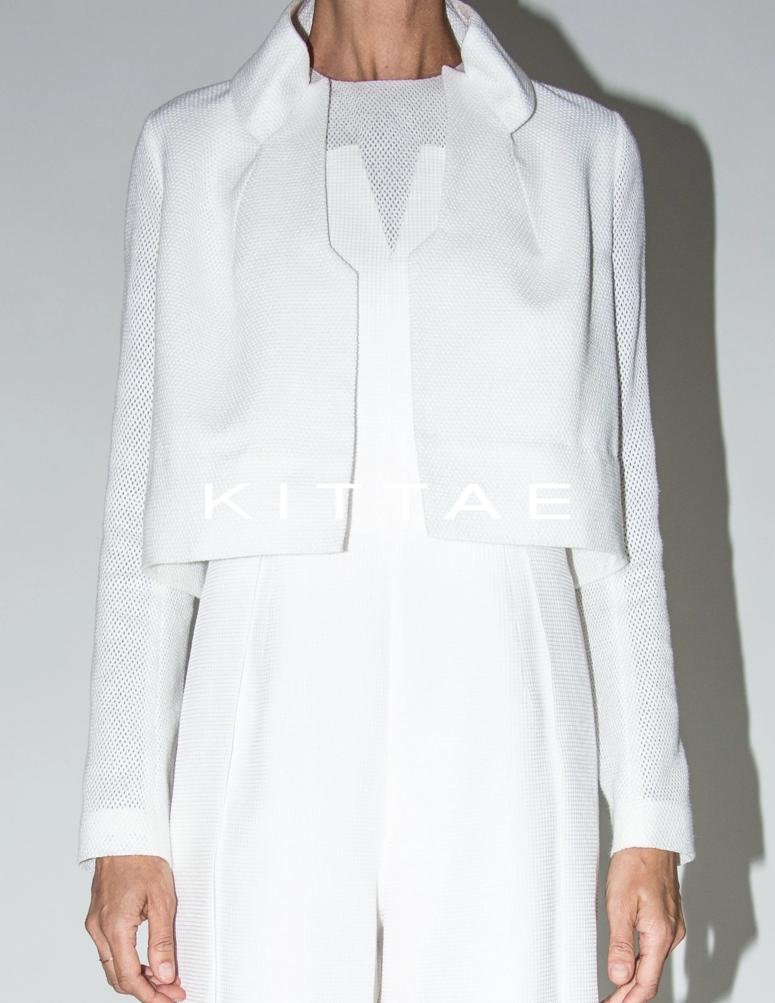 A person wearing a white textured jacket and matching white pants, standing against a plain background.
