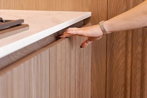 Person's hand reaching under a white countertop in a wooden cabinet.