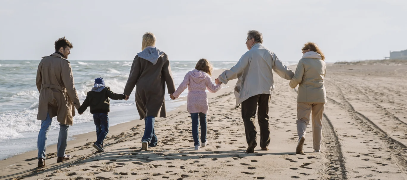 A family of all generations walking hand in hand on a beach