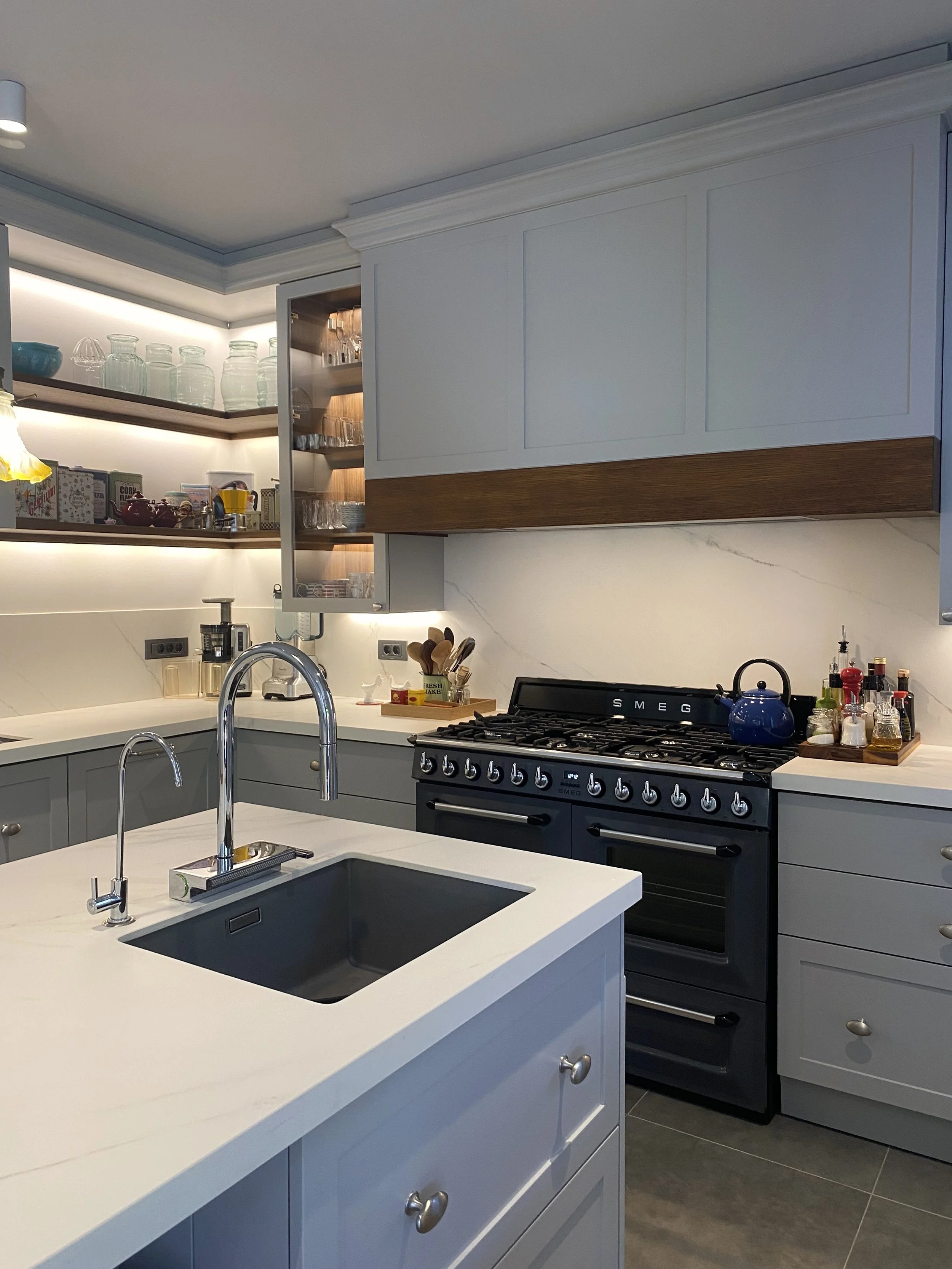 Eclectic modern kitchen featuring soft-grey lacquered HDF shaker cabinetry, warm wood accents, and a marble-veined Cosentino quartz backsplash, with integrated LED lighting. 