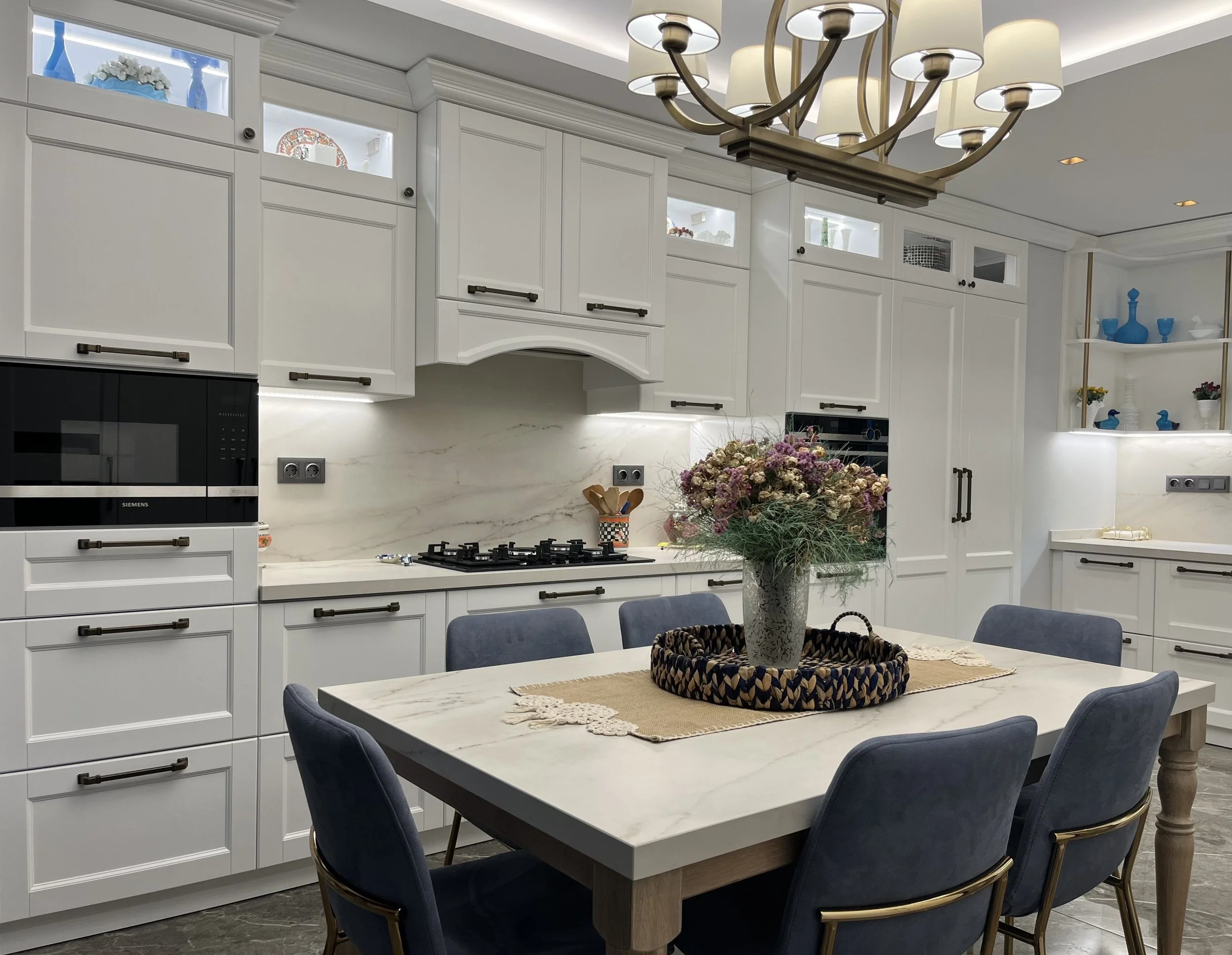 Bright open-concept kitchen featuring traditional shaker cabinetry and a central custom dining table with matching stone top.