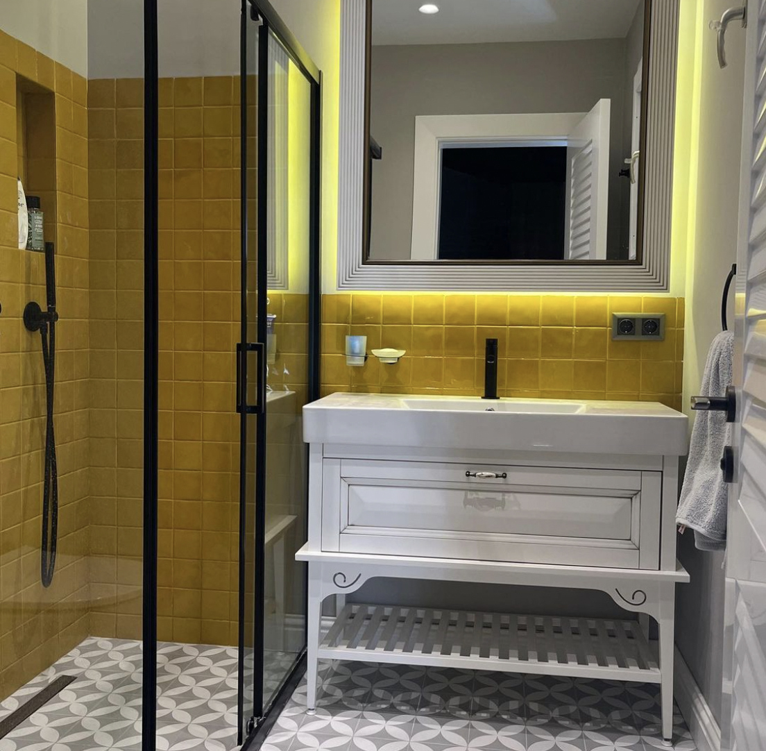 Elegant bathroom with mediterranean style mustard yellow wall tiles and grey white mosaic floor tiles. 