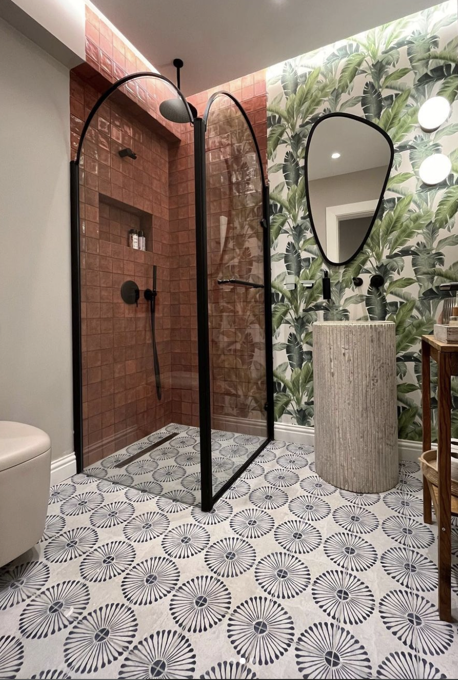 Elegant bathroom with mediterranean style cinnamon red wall tiles and blue white floor tiles, and tropical leaves design wallpaper.