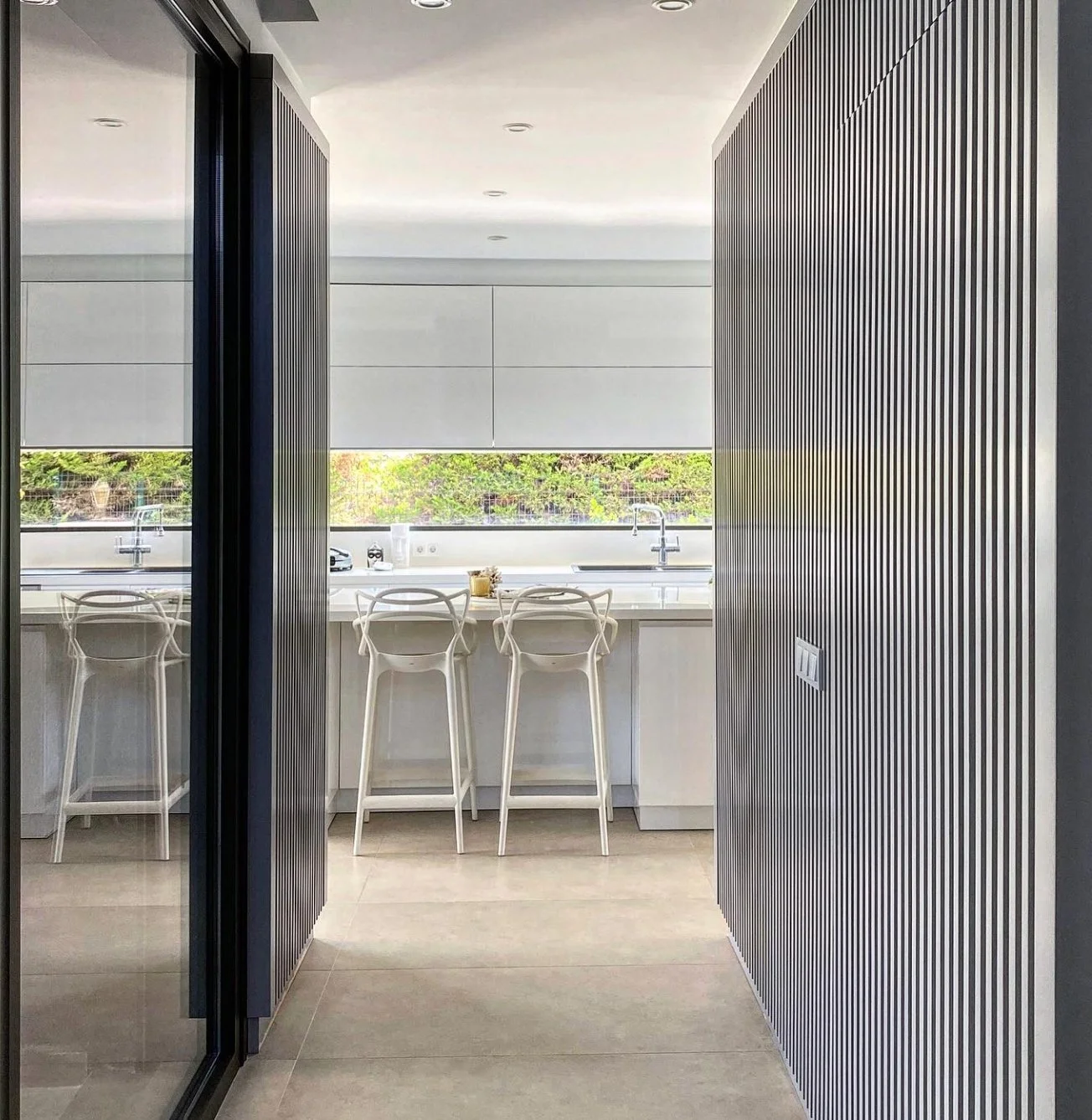Entrance to the modern minimalist kitchen with a combination of white plain and light blue-gray cabinets with vertical stripes.