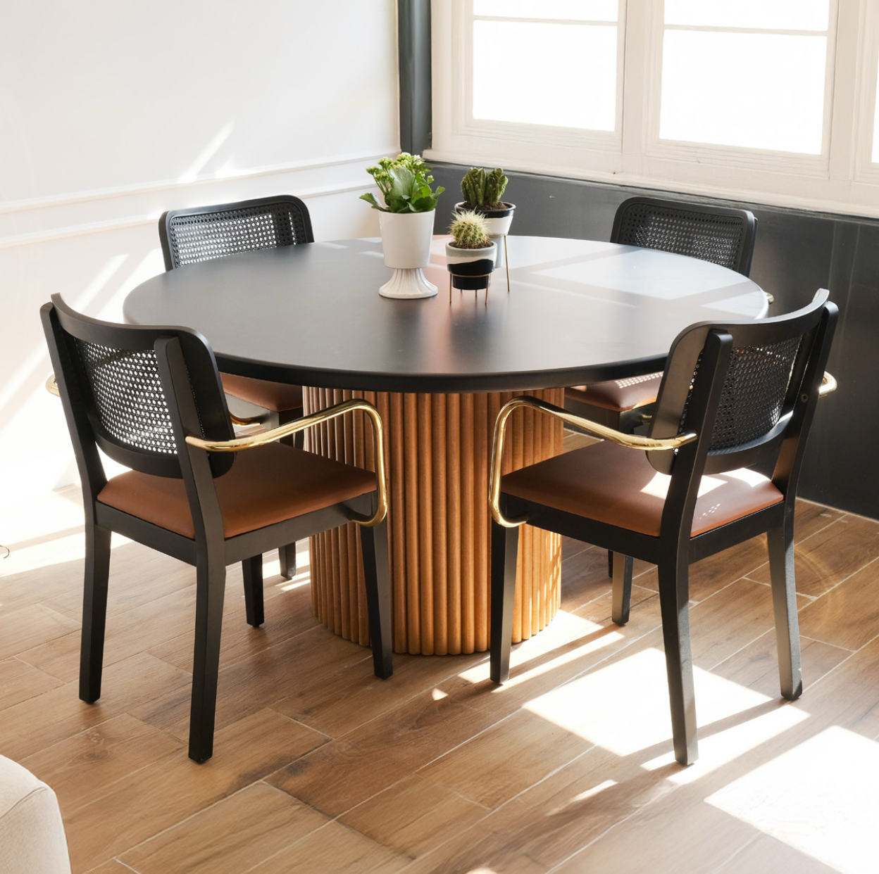 Luxury dining set featuring a black round table with a fluted wood pedestal base and NOMO black wooden chairs with brass armrests and leather seats.