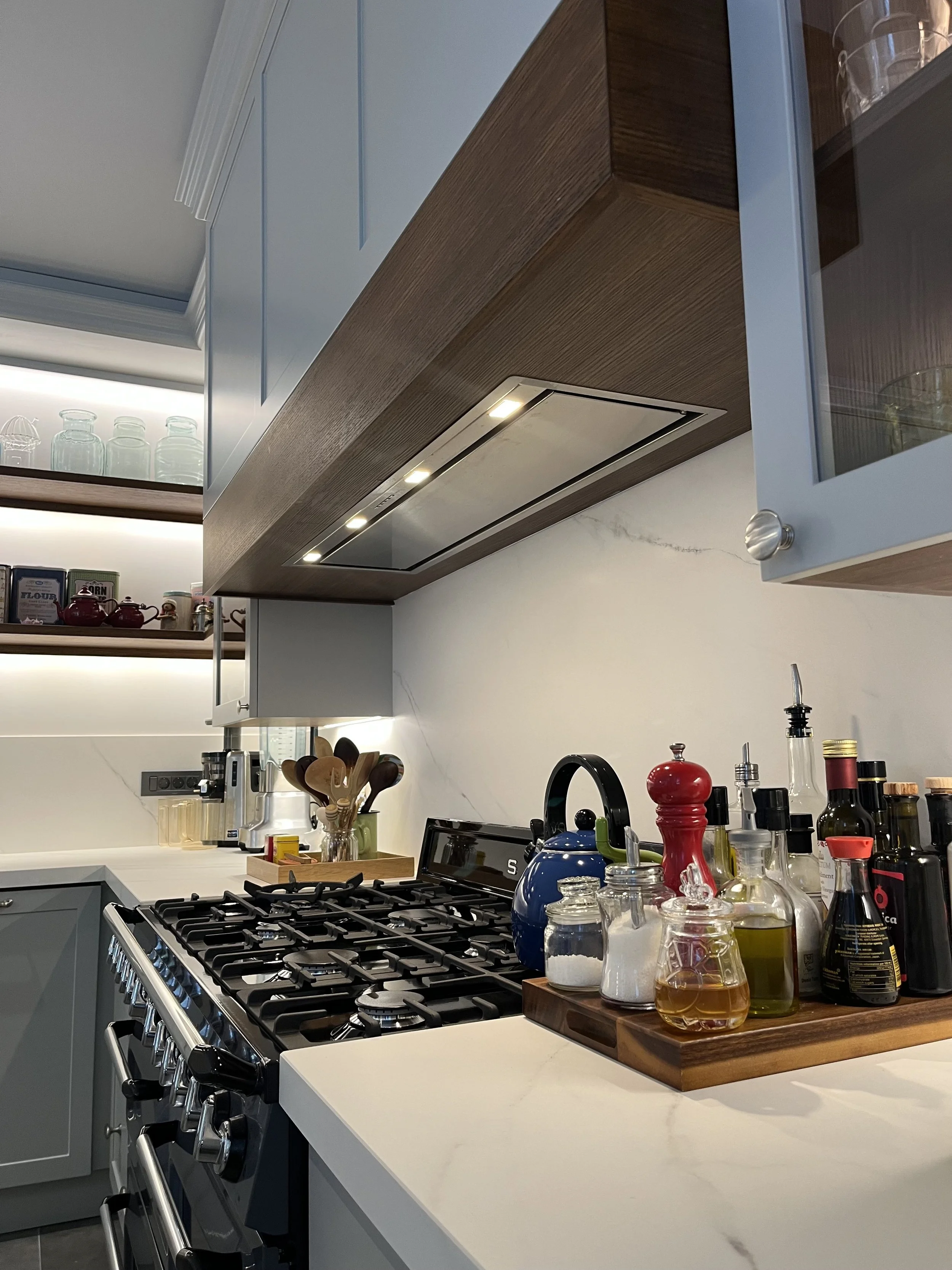 Eclectic modern kitchen featuring soft-grey lacquered HDF shaker cabinetry, warm wood accents, and a marble-veined Cosentino quartz backsplash, with integrated LED lighting. 