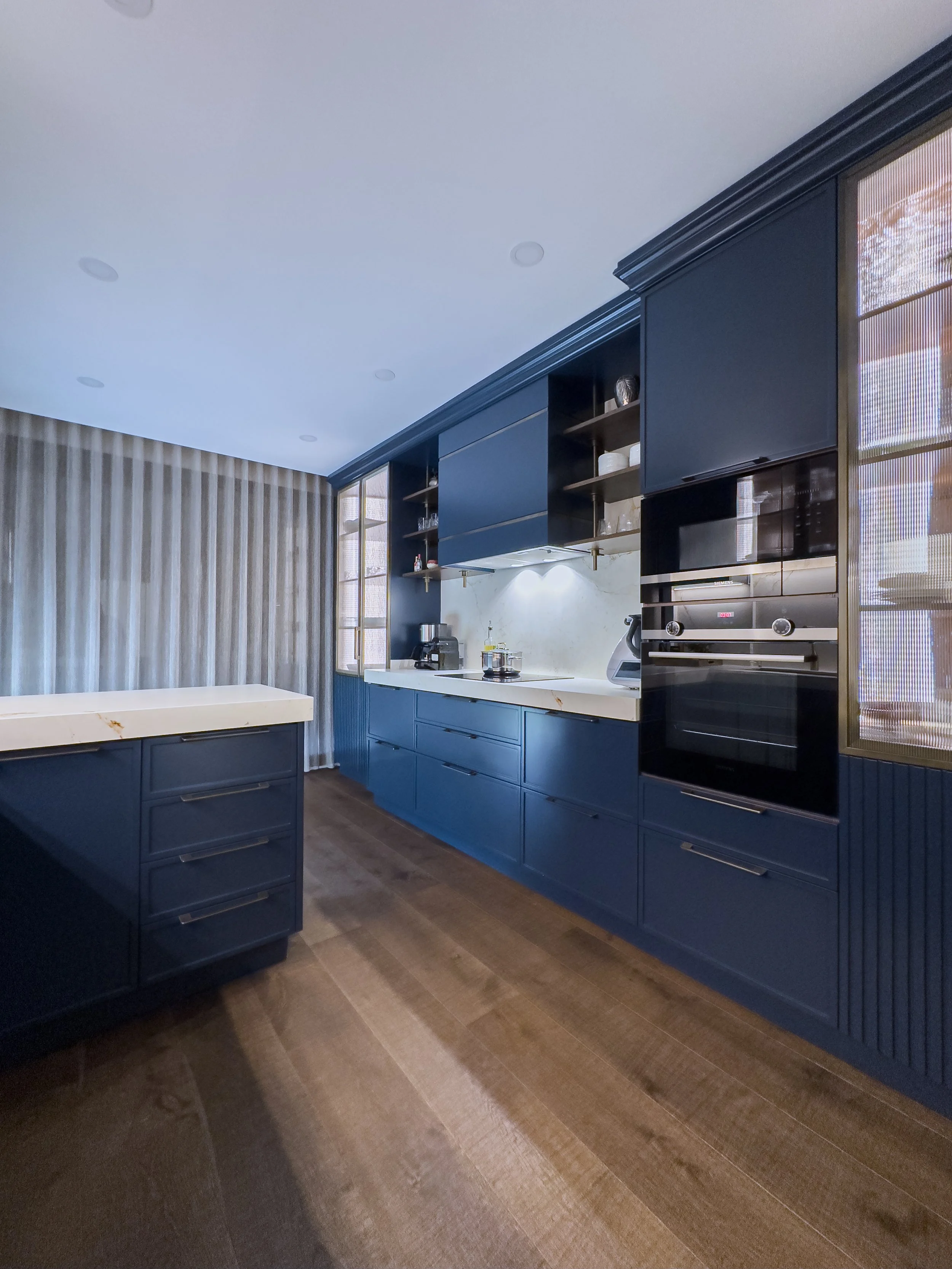 Marine-blue lacquer custom kitchen cabinets with fluted detailing, white quartz countertops and brass hardware – modern luxe kitchen by NUOVO Kitchens Vancouver.