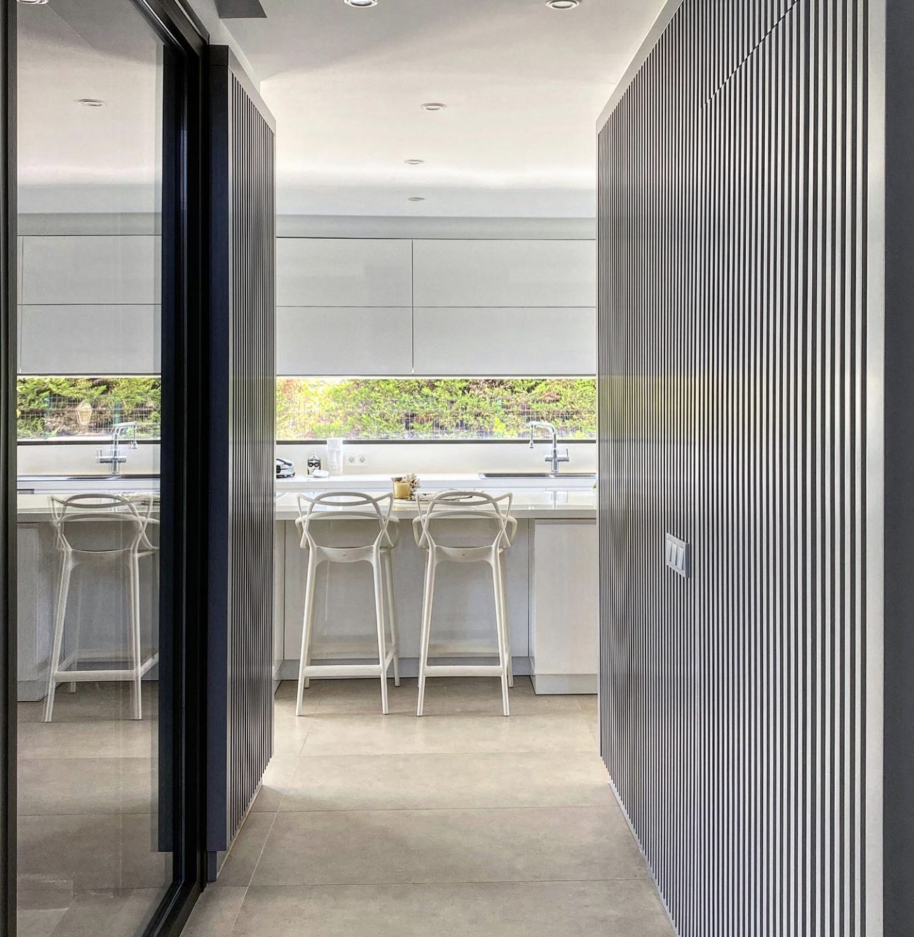 Ultra-modern fluted kitchen with custom vertical slatted cabinet doors, integrated appliances and a bright white island, crafted by Nuovo Kitchens in Vancouver.