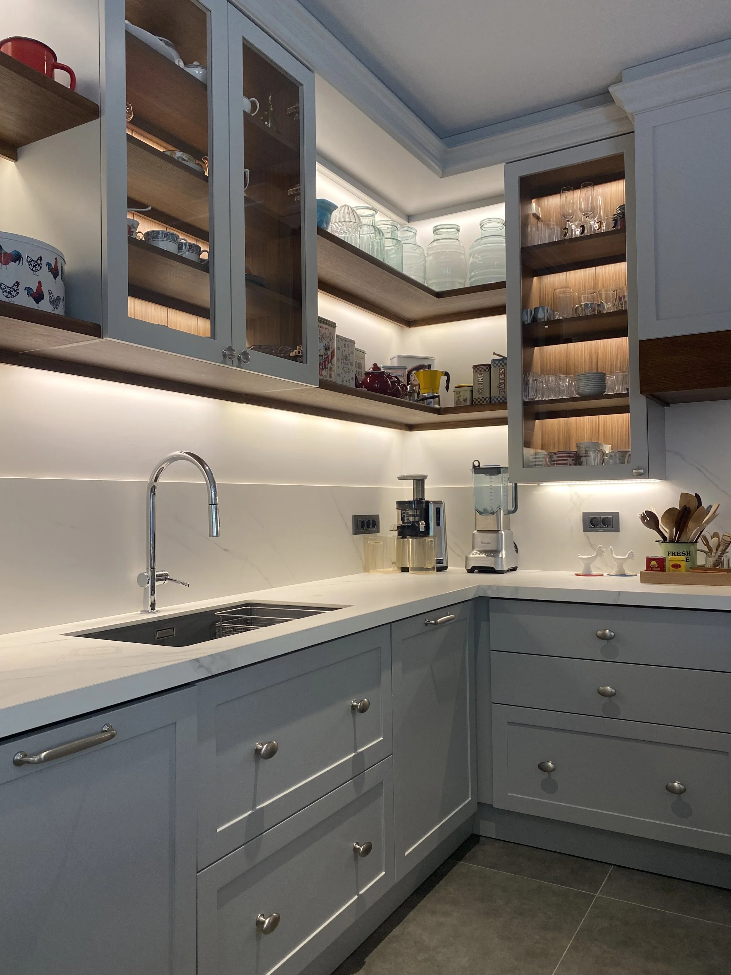 Eclectic modern kitchen featuring soft-grey lacquered HDF shaker cabinetry, warm wood accents, and a marble-veined Cosentino quartz backsplash, with integrated LED lighting. 