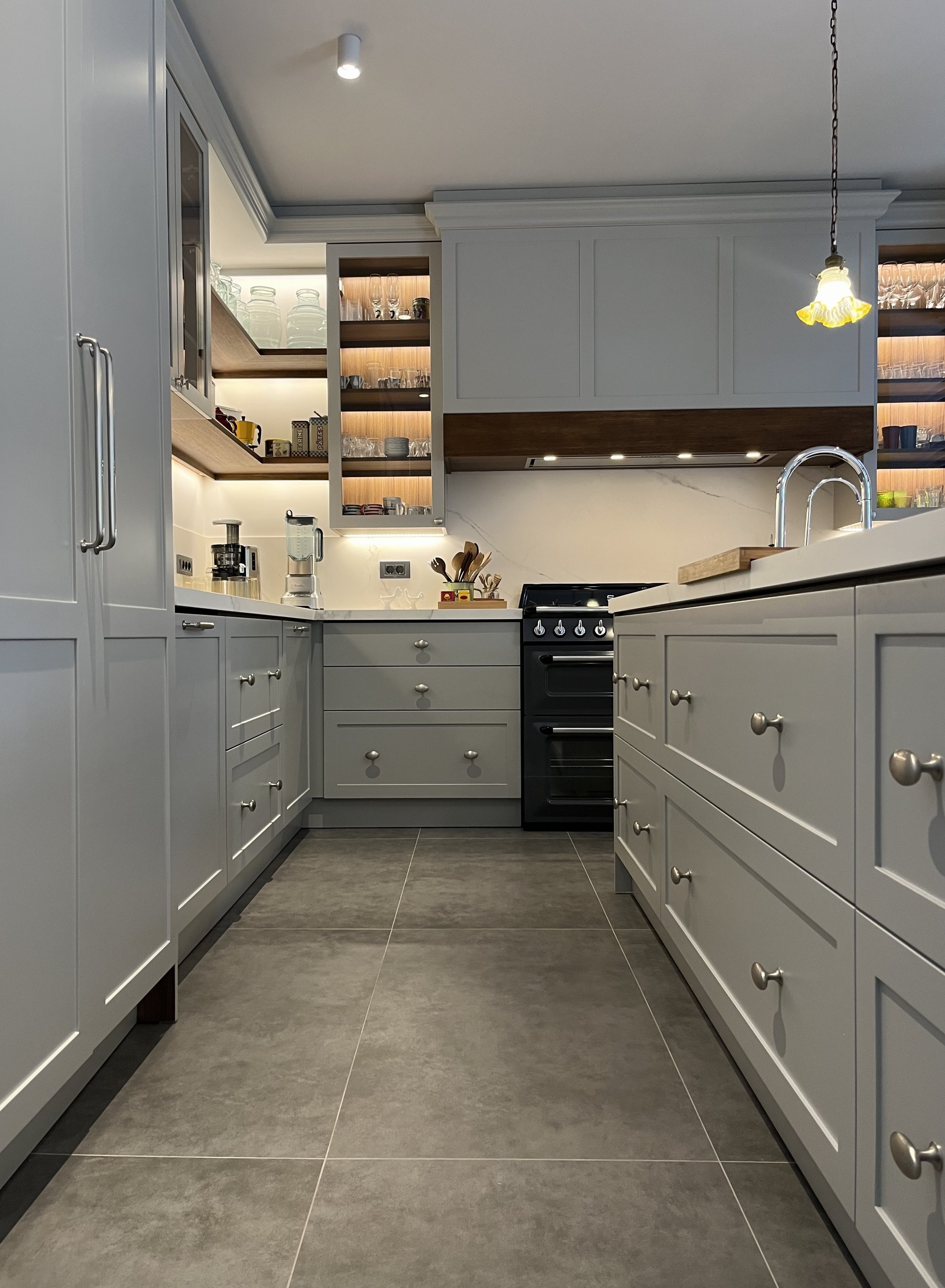 Eclectic modern kitchen featuring soft-grey lacquered HDF shaker cabinetry, warm wood accents, and a marble-veined Cosentino quartz backsplash, with integrated LED lighting. 