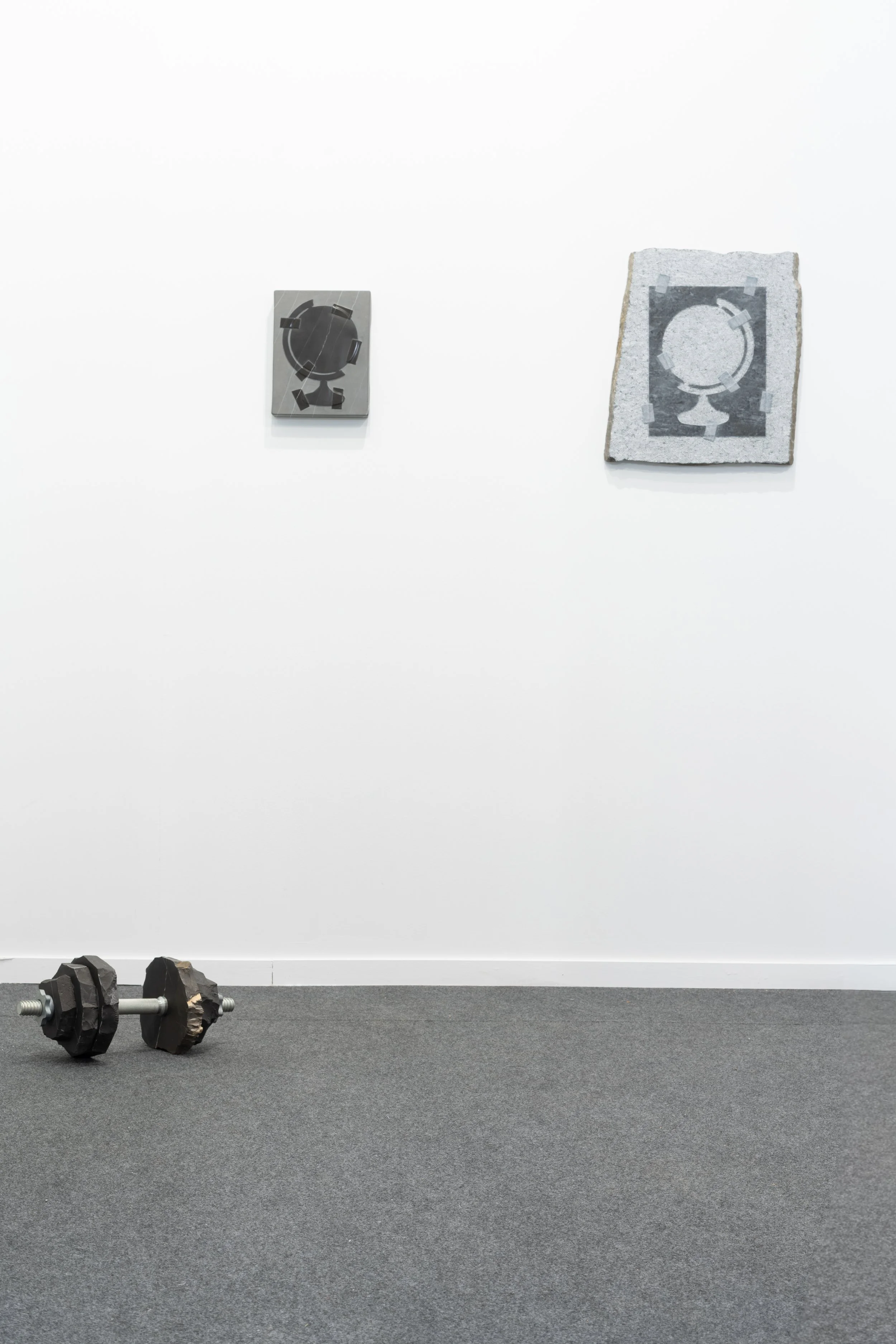 Gym with a pair of dumbbells on the floor, a weight lifting barbell, a white wall, and framed artwork hanging on the wall.