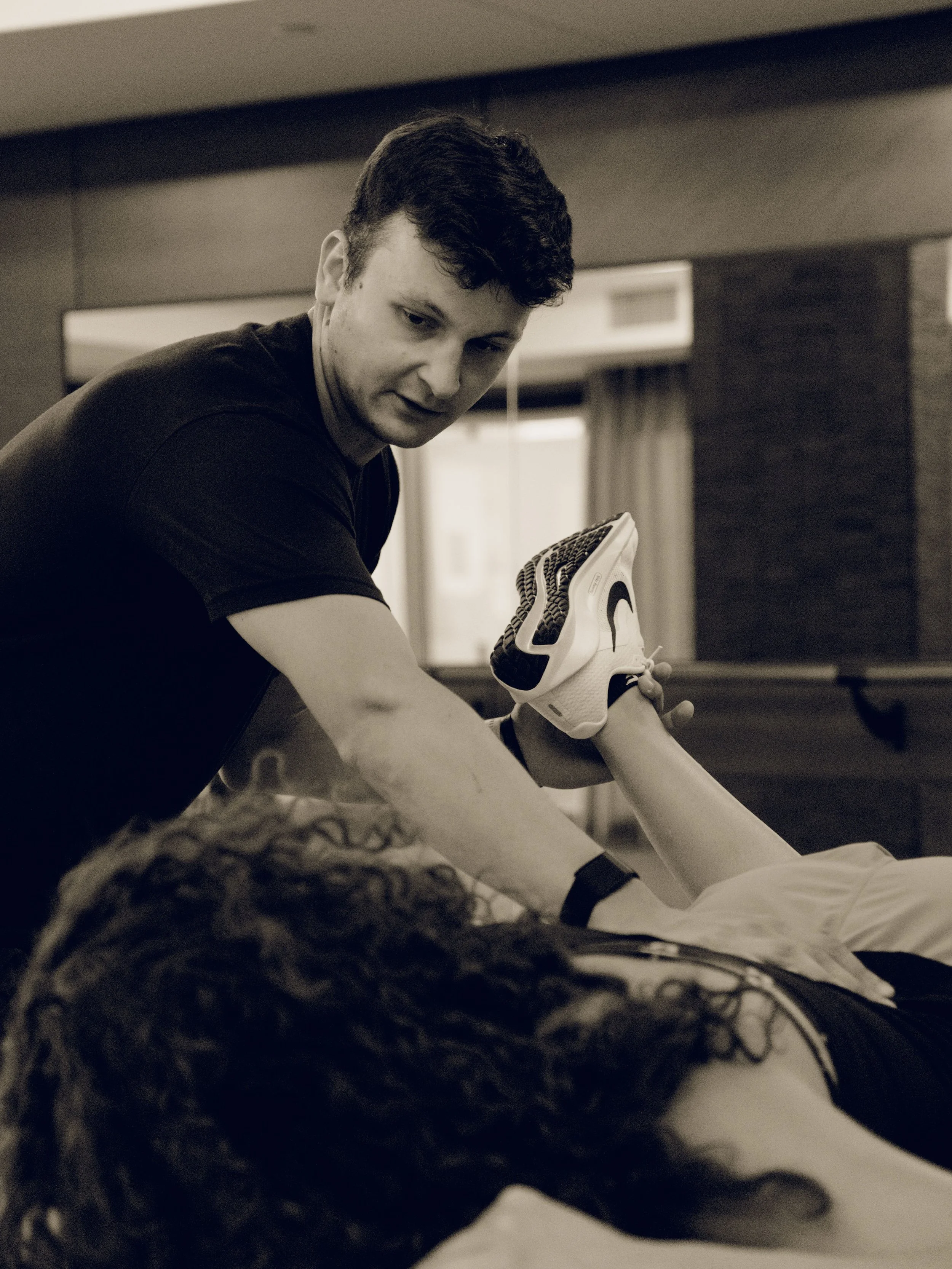 A young man providing CPR training to a woman lying on a table, with another person supporting her leg during the demonstration.