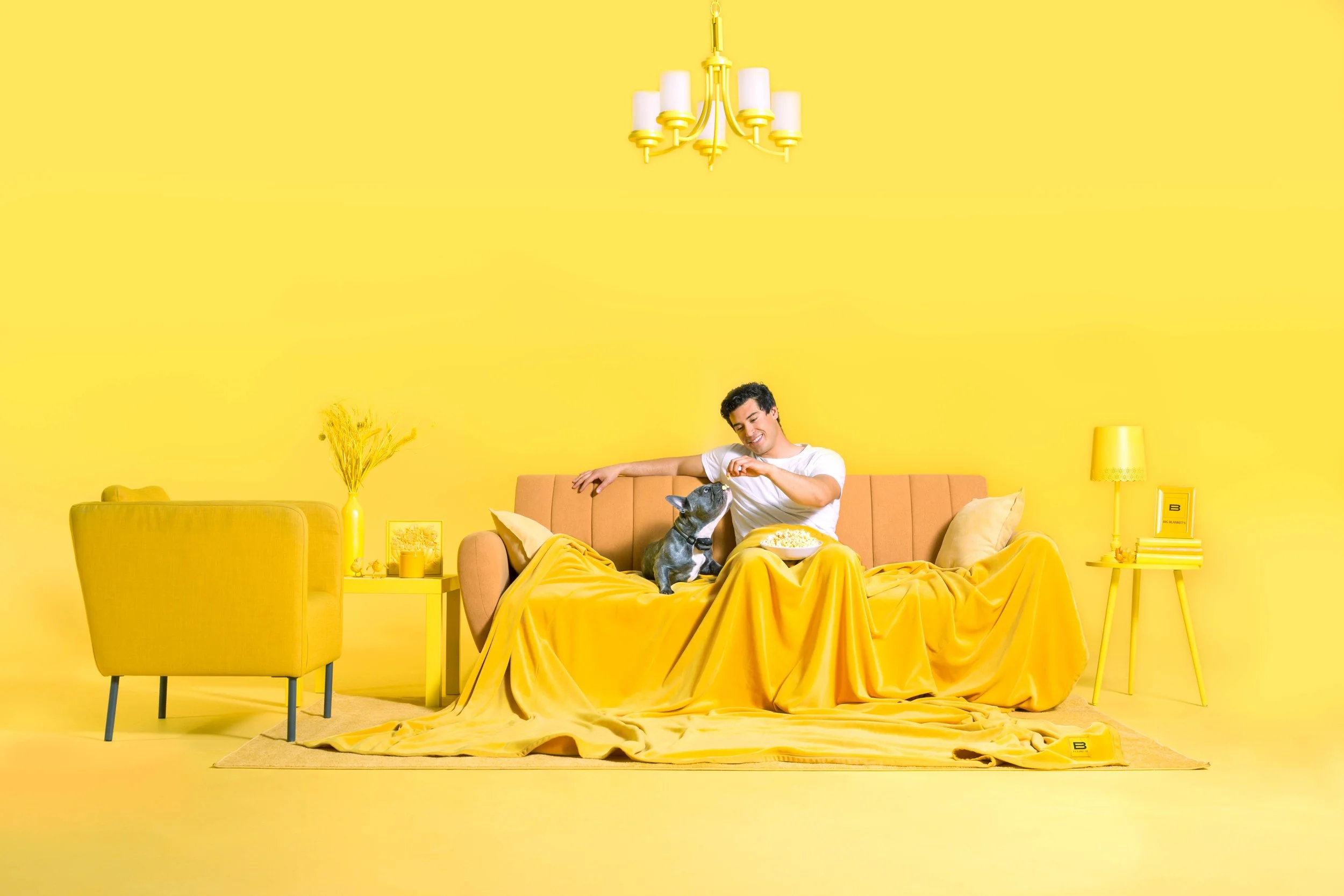 A woman wearing a hat adjusts Roman shades in a cozy living room with turquoise walls. There's a dark blue sofa with pillows, a white shelf with books and decor, and a framed botanical print on the wall. Emmerson Studios, Photographed by Emmie Edmo