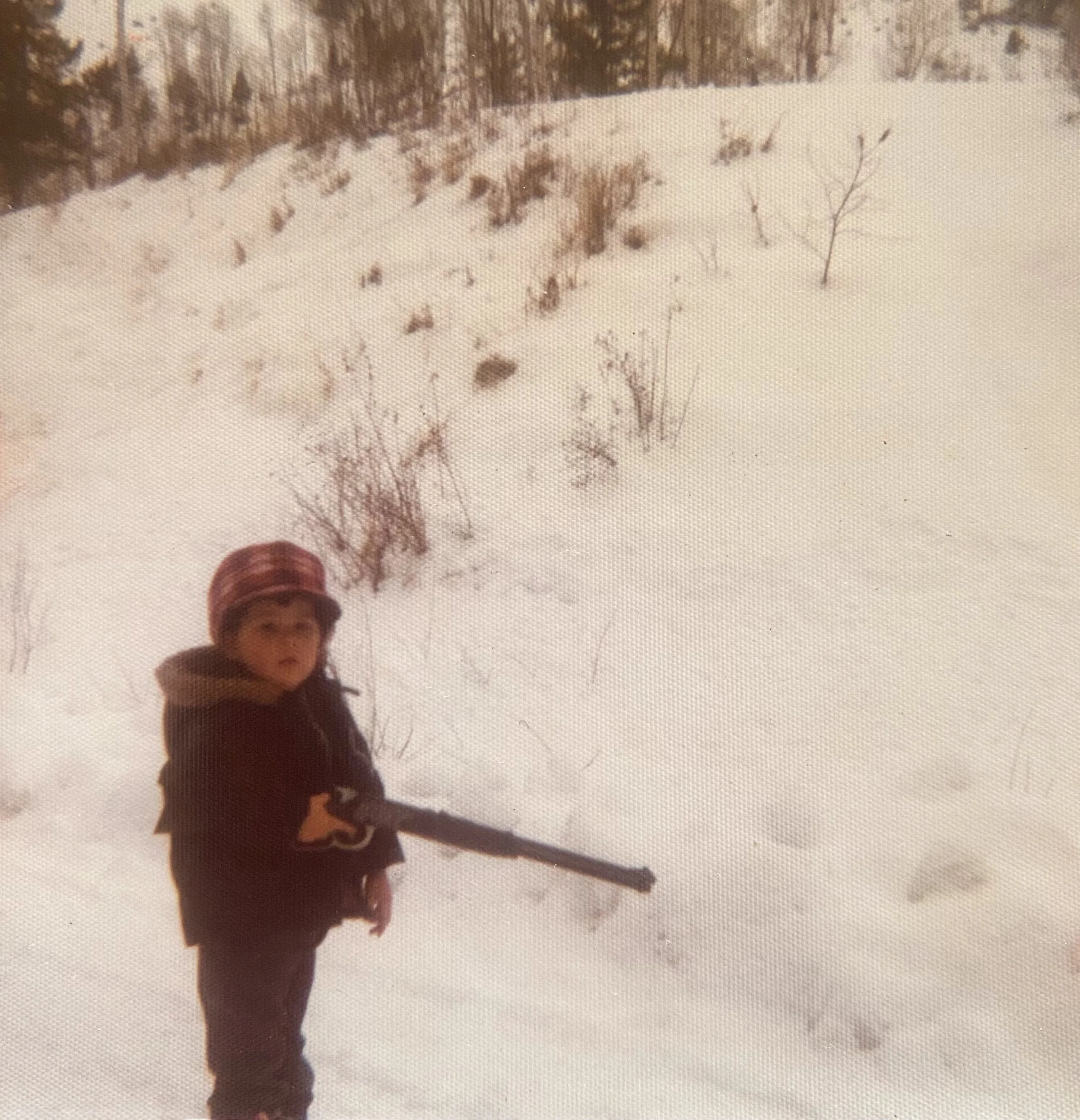 A young boy in winter clothing and a hat holding a stick in a snowy outdoor setting. Emmie Edmo's family