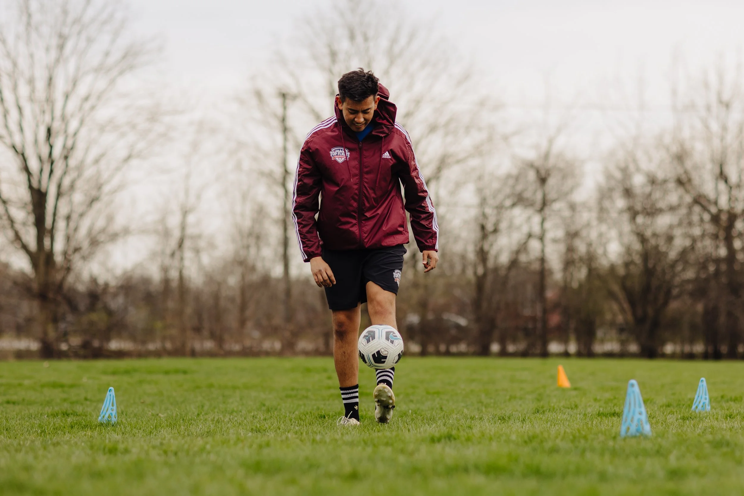 Man practicing soccer outdoors on a grassy field with training cones and a ball.