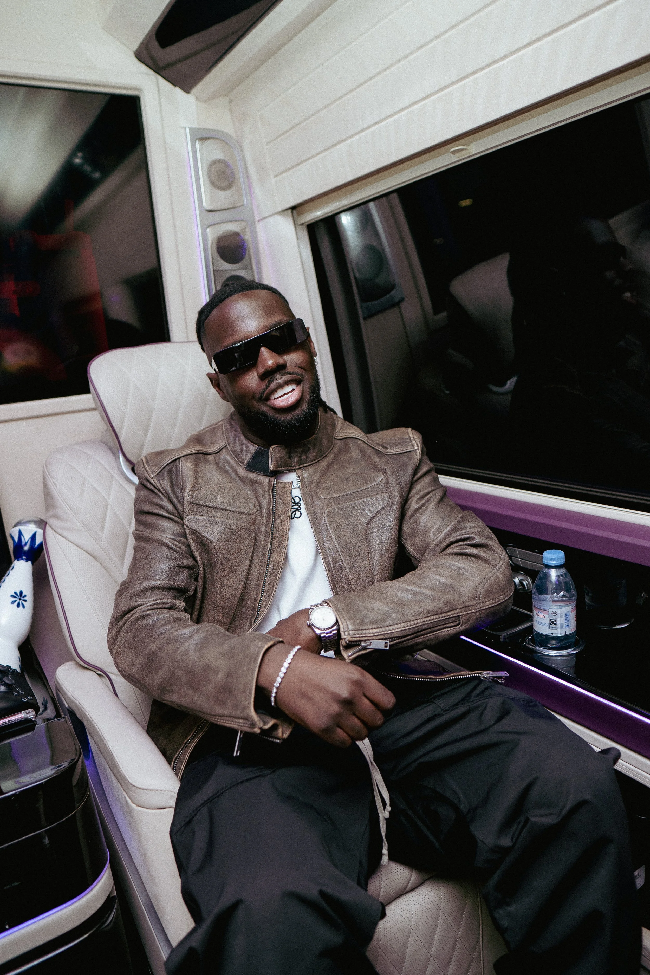 Un homme en vêtements décontractés, portant des lunettes de soleil, assis dans un siège de luxe dans un véhicule.