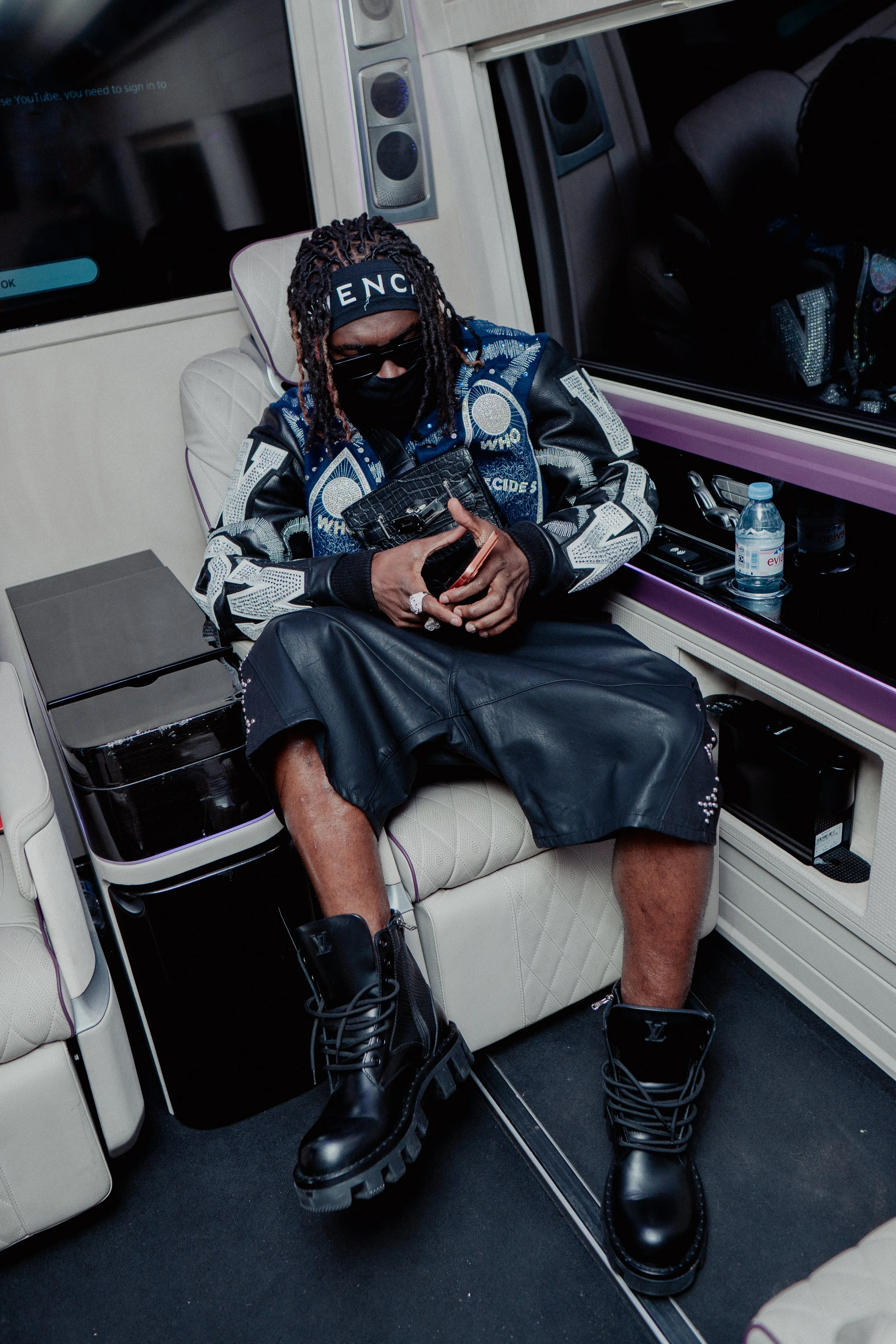 Une personne portant des vêtements de mode, assise dans un véhicule, utilisant un téléphone portable.