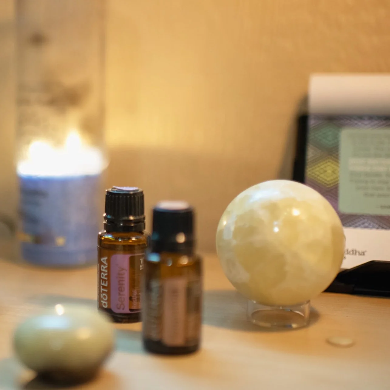 Essential oils bottles, a moon lamp, and candles on a wooden surface.