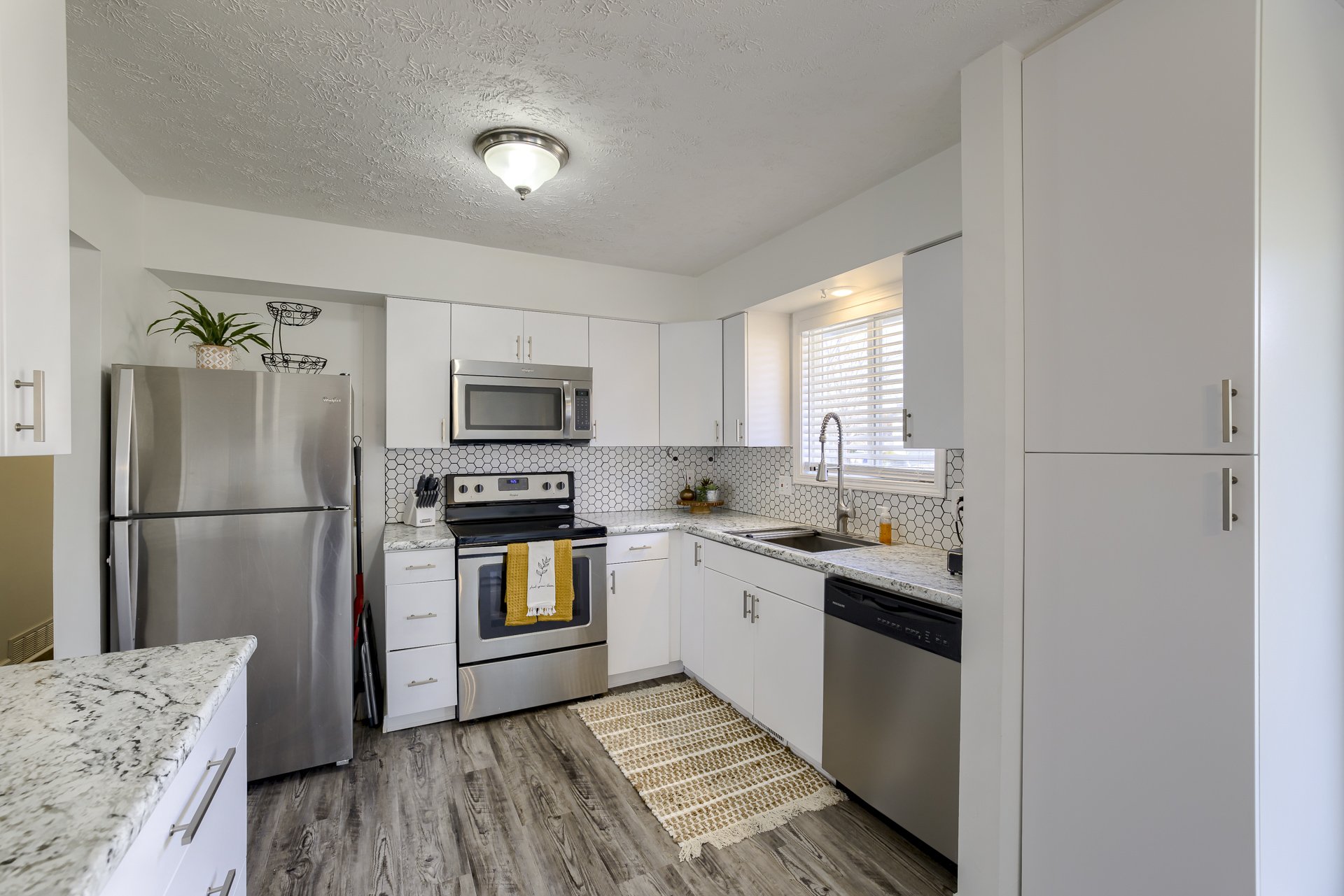 Kitchen with white cabinets, stainless steel appliances, a granite countertop, and a window with blinds.