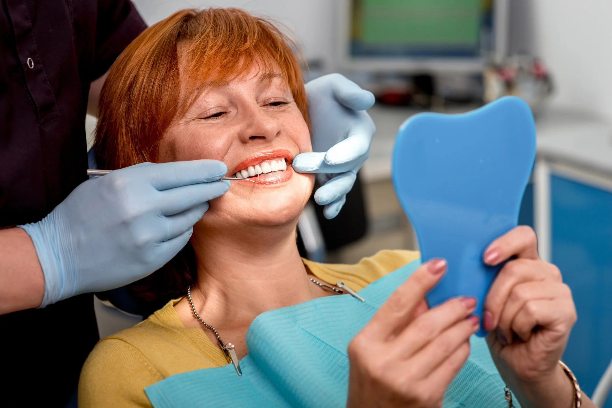 2nd visit. Woman at dentist's office holding a mirror looking at her newly build denture. Dentures Preston. Dentures Frankston.