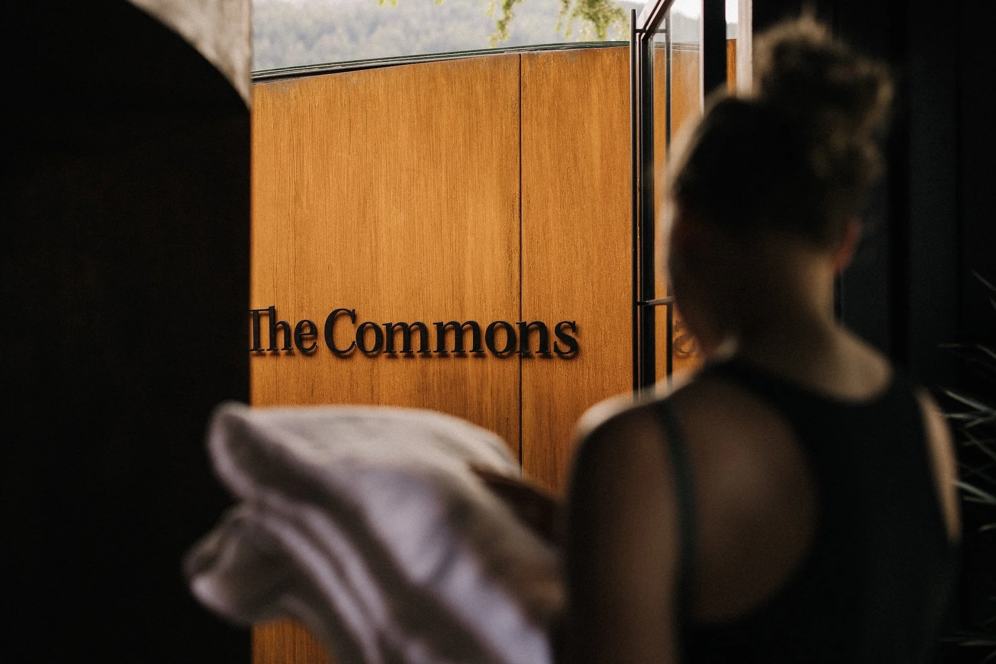 A bather holding towels walking towards the entrance for The Commons Communal hot pool at Bathe Hot Pools Queenstown.