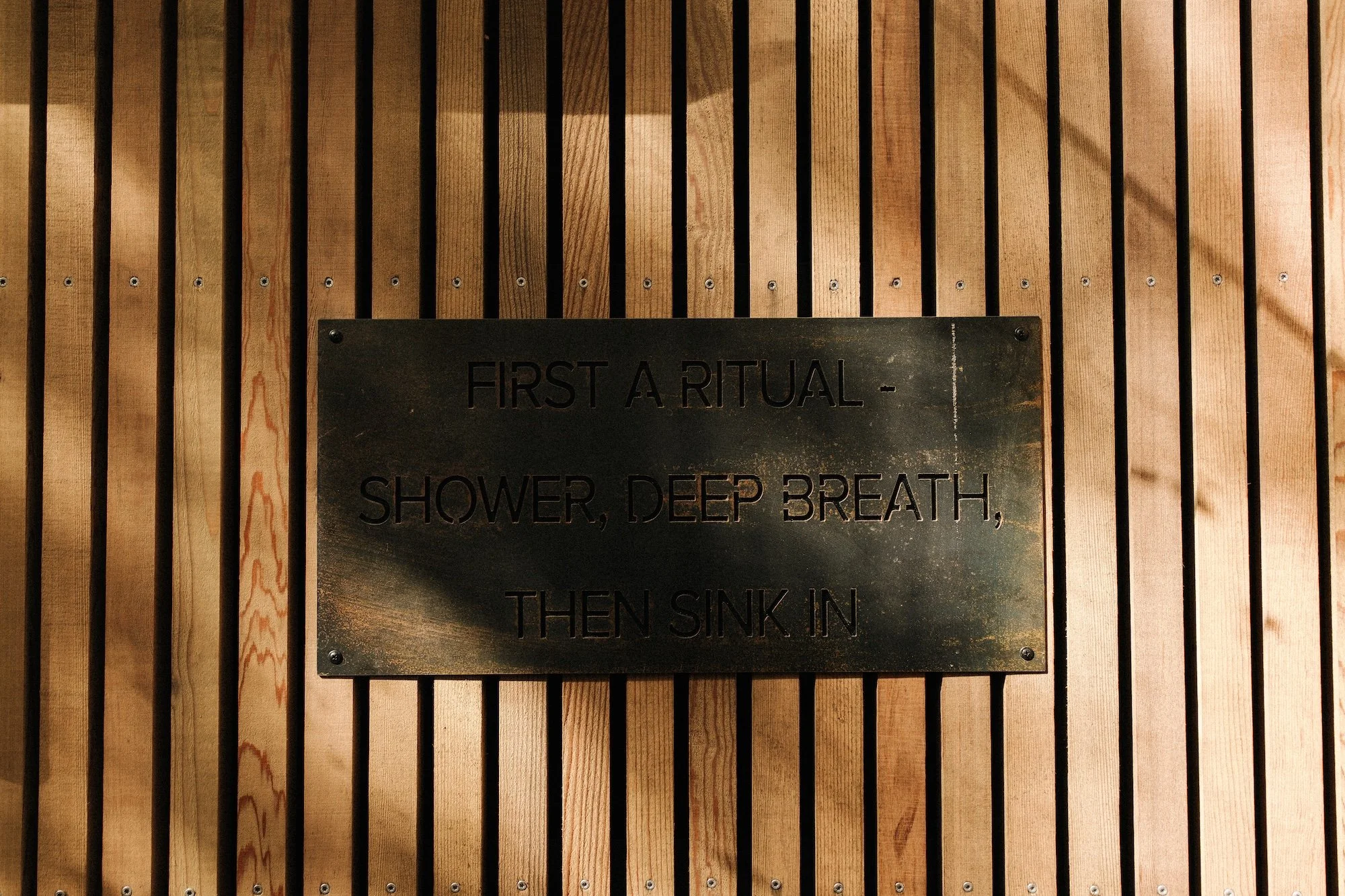 A steel sign outlining the Bathe soak. 'First a ritual, Shower, Deep Breath, then sink in.'