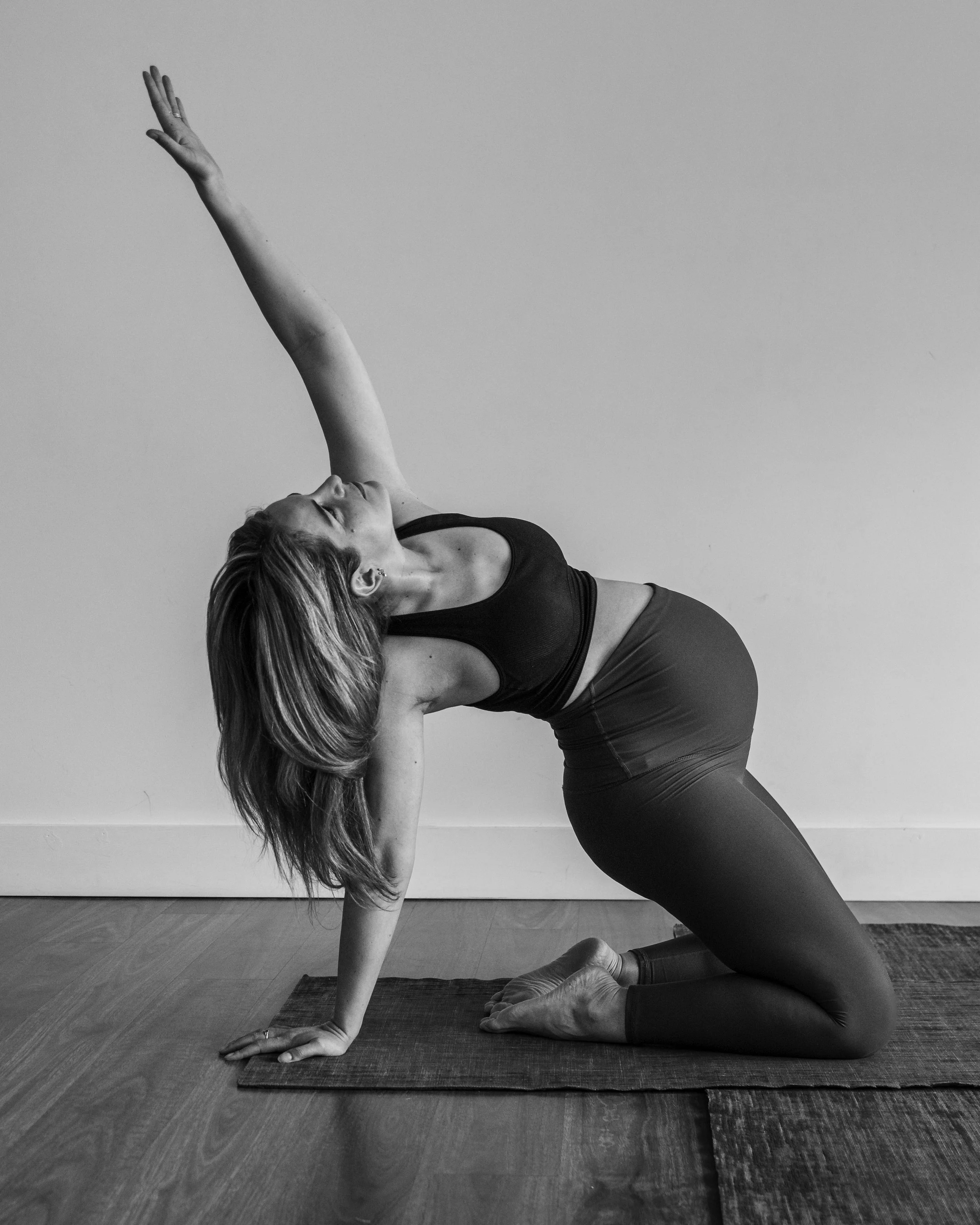 Black and white picture of pregnant woman in full bloom, practicing pregnancy yoga in a modified camel pose