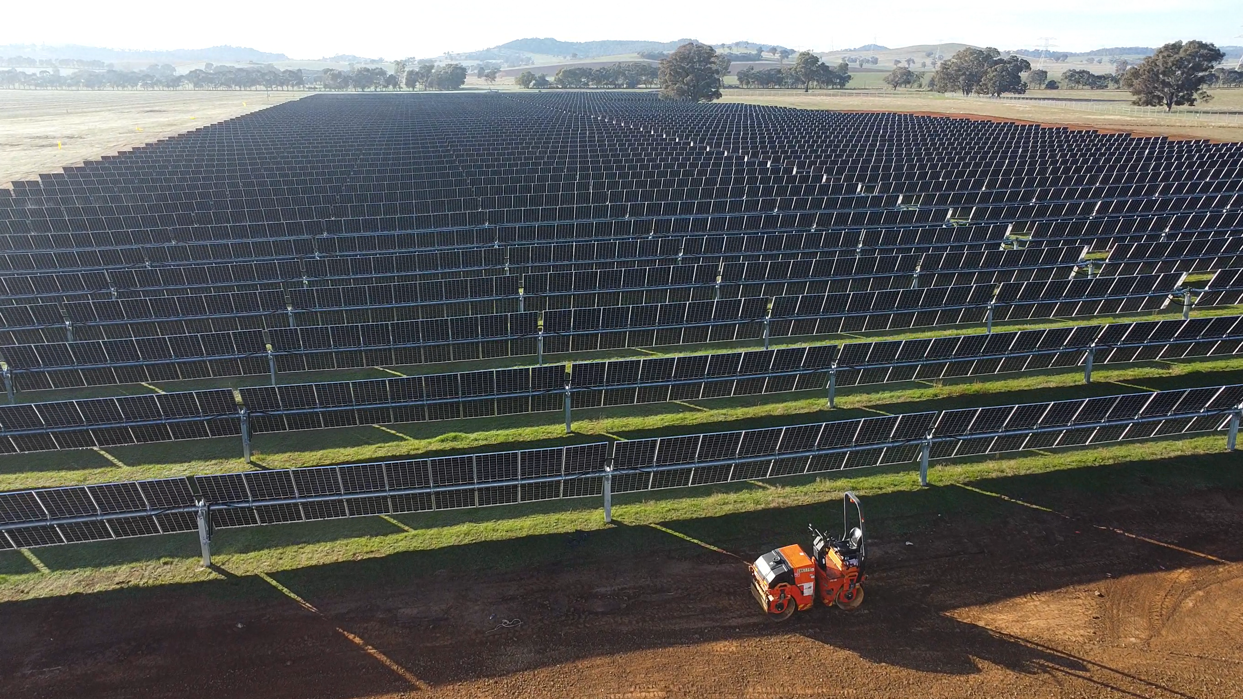 CleanPeak Energy operated Uranquinty solar farm, showing numerous solar panels installed on a field, with some ground work and equipment in the foreground, and a rural landscape with trees and hills in the background.