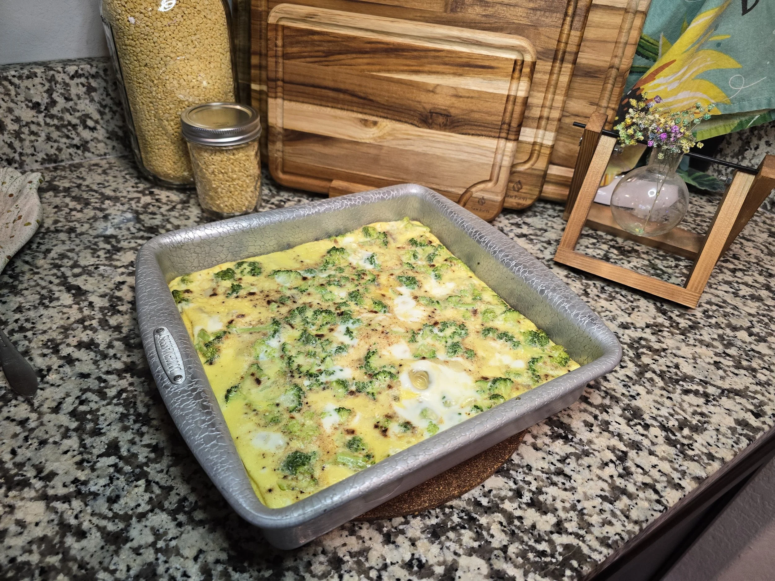 Potato and broccoli breakfast casserole baked in a square pan with golden eggs and melted cheese on a kitchen countertop