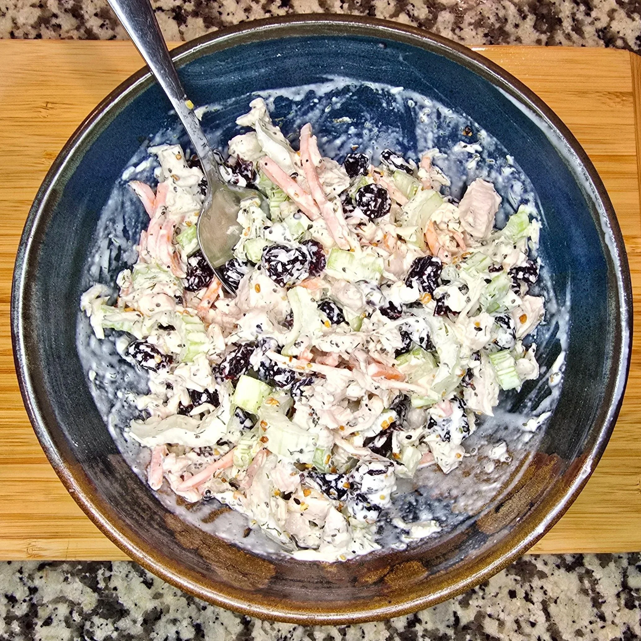cranberry avocado chicken salad with celery, carrots, dill, and everything bagel seasoning in a blue and red ceramic bowl on a wooden cutting board