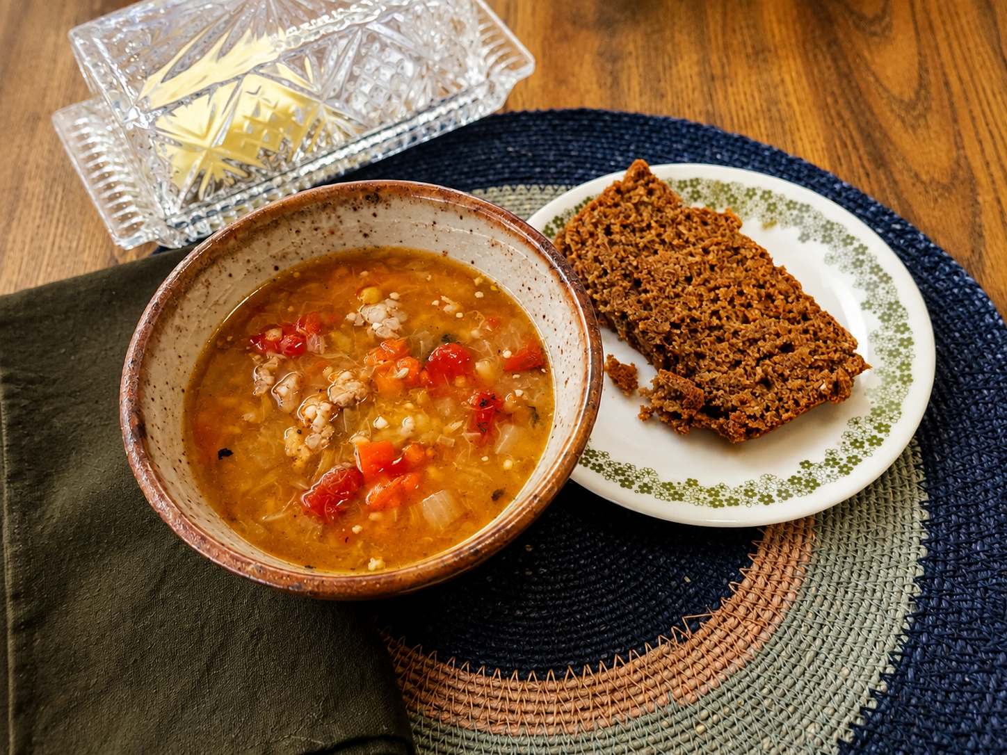 A rustic bowl of butternut squash soup with Italian sausage and vegetables served alongside a slice of hearty bread on a warm wooden table.