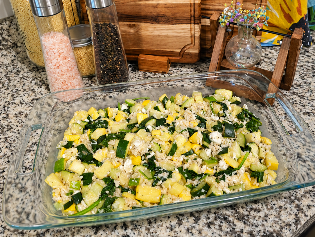 Mediterranean zucchini, yellow squash, and spinach bake topped with feta and Parmesan in a white baking dish.