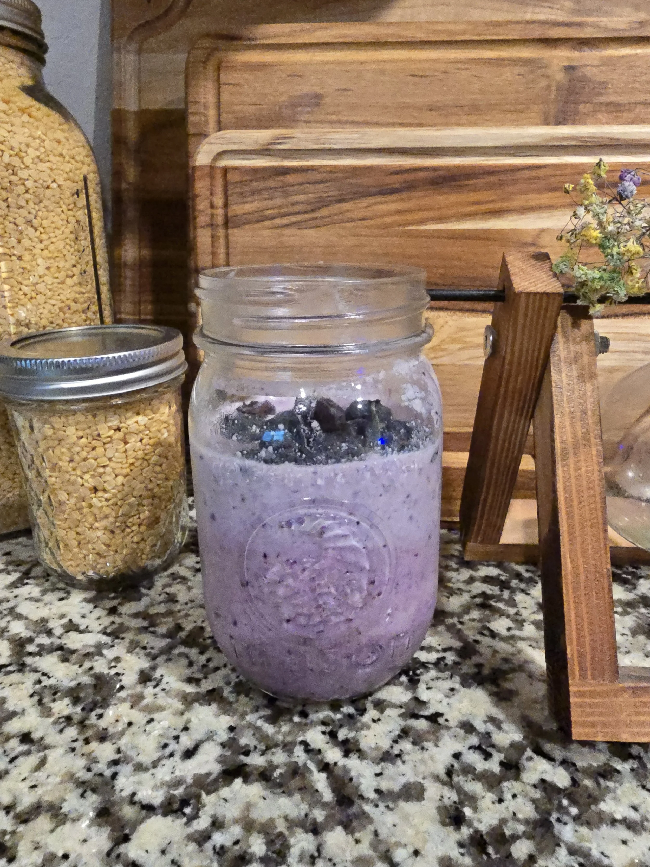 Strawberry Blueberry Oatmeal Smoothie with Chia Seeds and Collagen in a mason jar on a granite counter top and flowers.