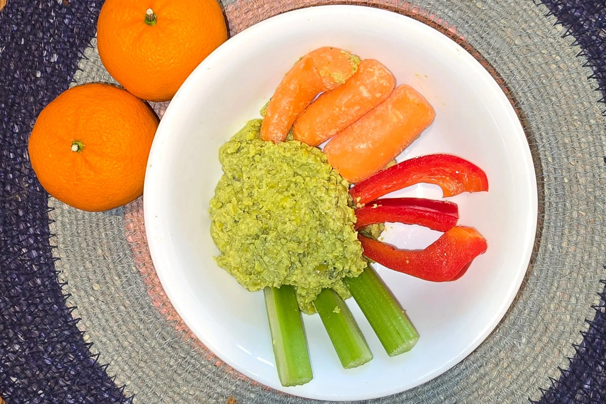 Green pea pesto in a white bowl with carrots, red peppers, celery, and clemontines