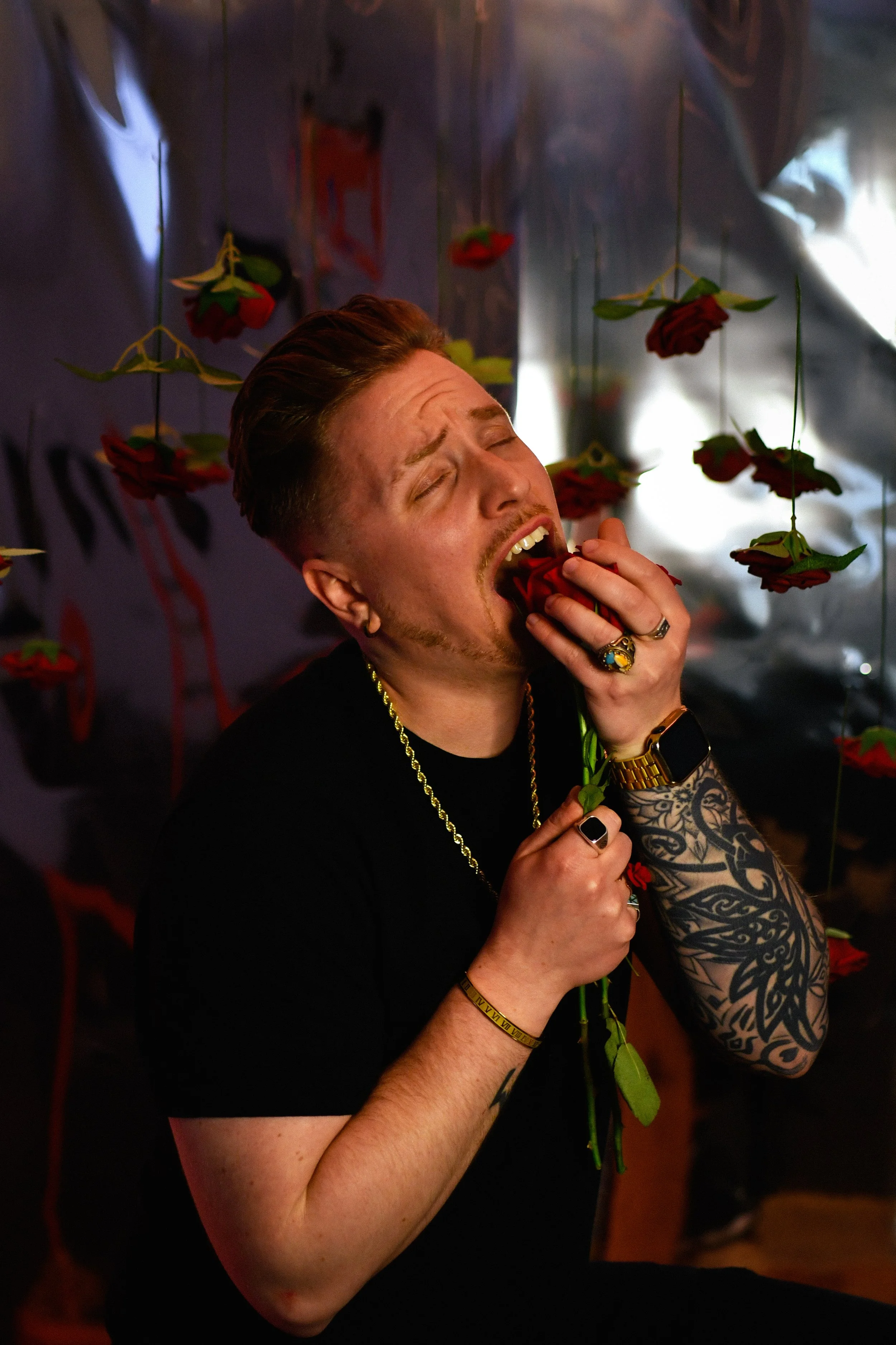 Grayson Rose eating Rose. Man eating biting shoving down a rose in his throat with roses in the background.