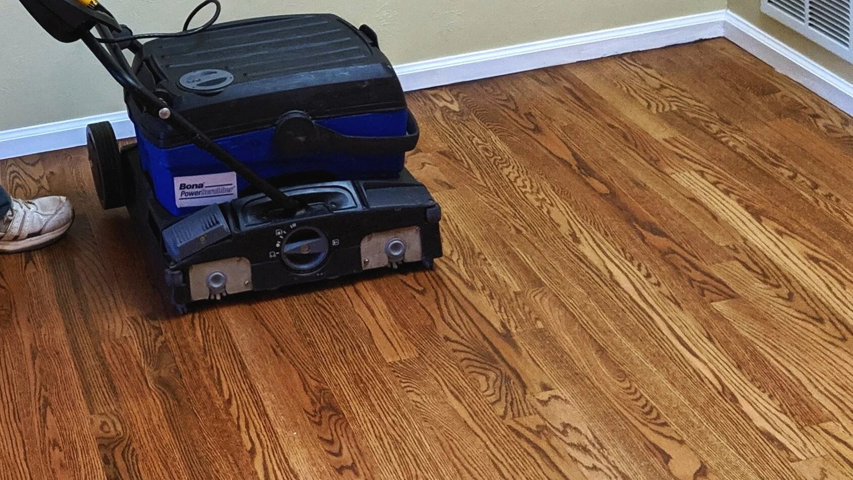 hardwood floor machine on beautiful hardwood floor with gorgeous wood grain design. There is a shoe in the left of hte image where the operator of the machine is standing.