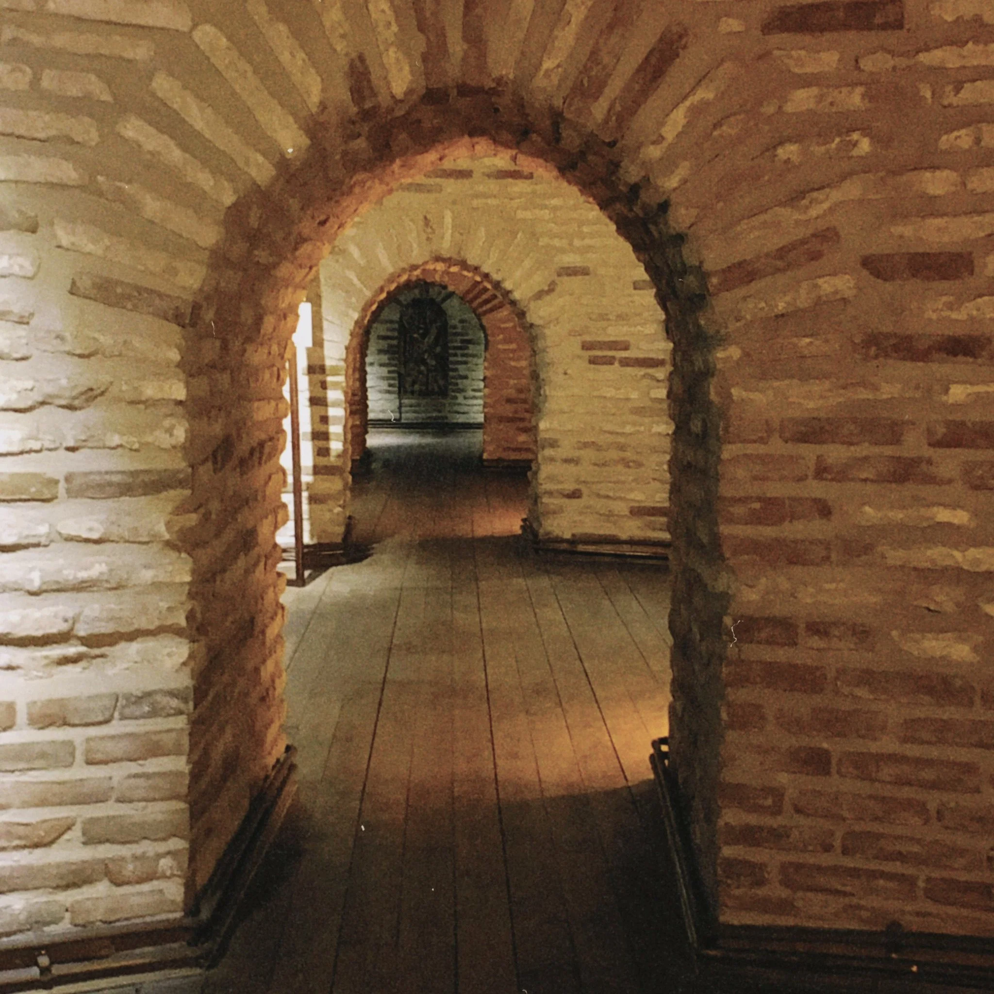 view of a medieval home with brick walls and three brick archways made with old, fading brick. The floor is lined with classic, old hardwood floors that line the walkway.