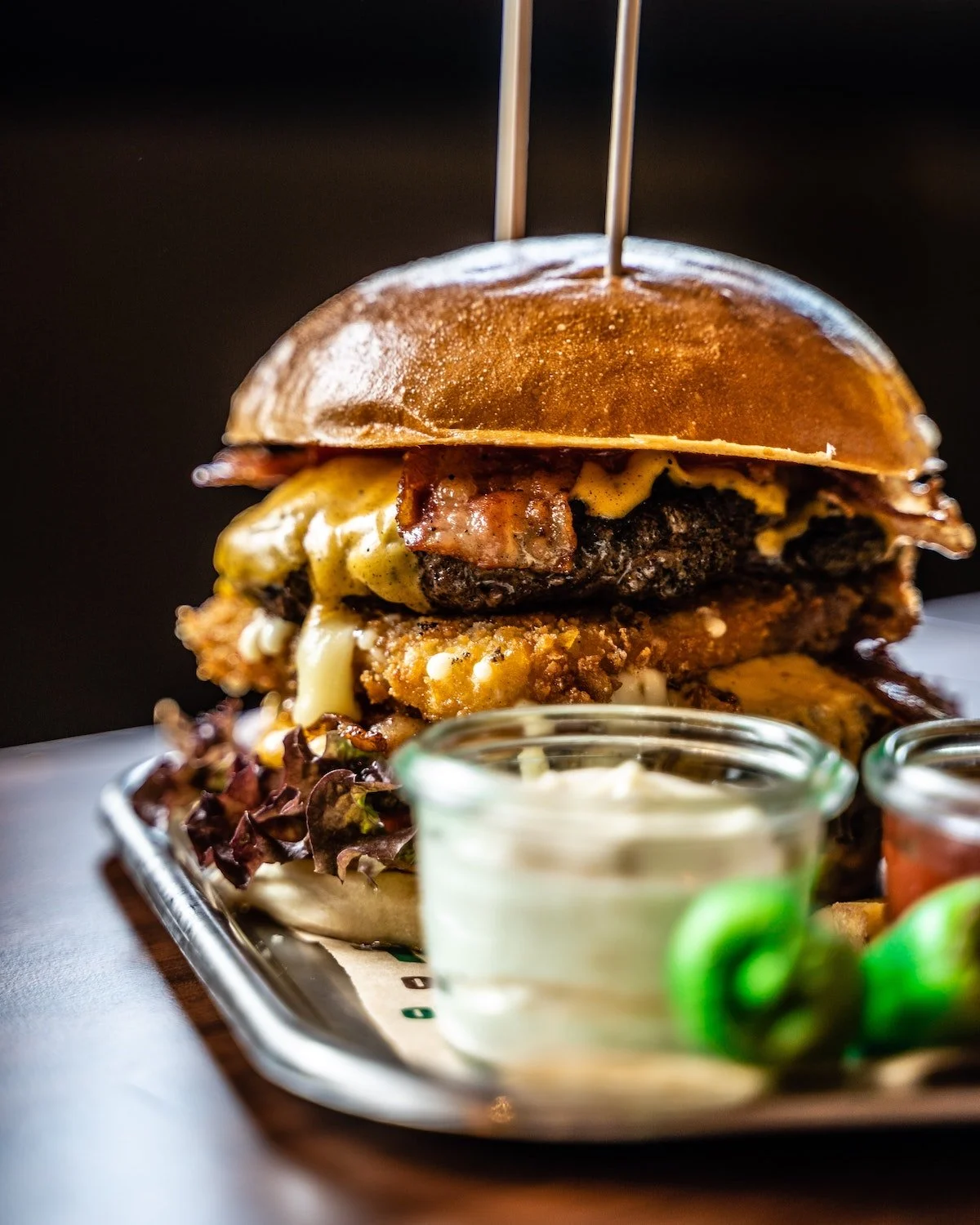 Towering gourmet cheeseburger with onion rings and dipping sauces at a Mt. Hood restaurant near RAVN HAUS modern alpine vacation rental in Government Camp, Oregon, highlighting local dining and après-ski