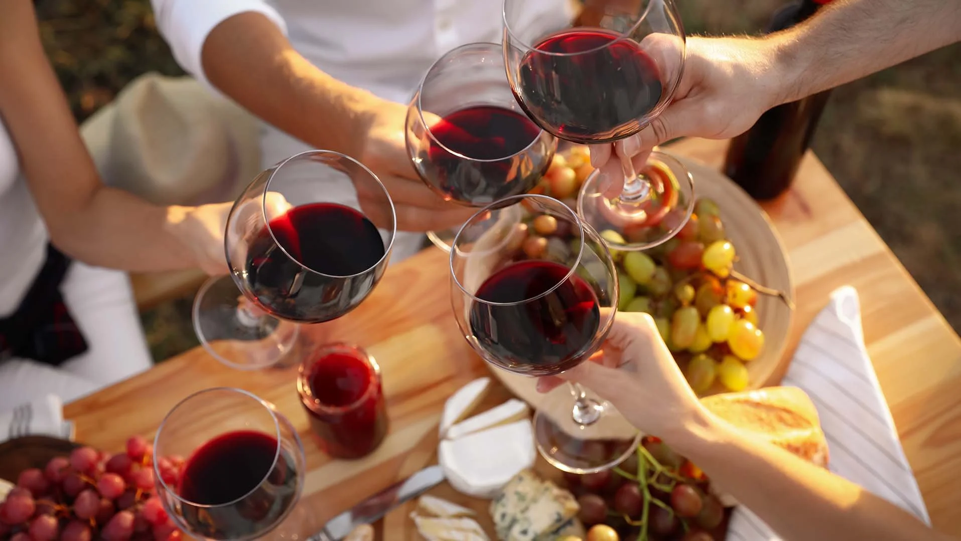 Group of friends toasting red wine glasses over a charcuterie board with grapes and cheese during a Mt. Hood wine tour near RAVN HAUS modern alpine vacation rental in Government Camp, Oregon.