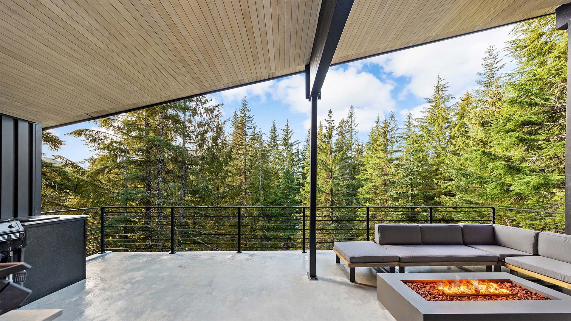 Cornice Deck at RAVN HAUS Mt. Hood vacation rental with covered treetop patio, modern fire pit, and cozy lounge seating above the forest.