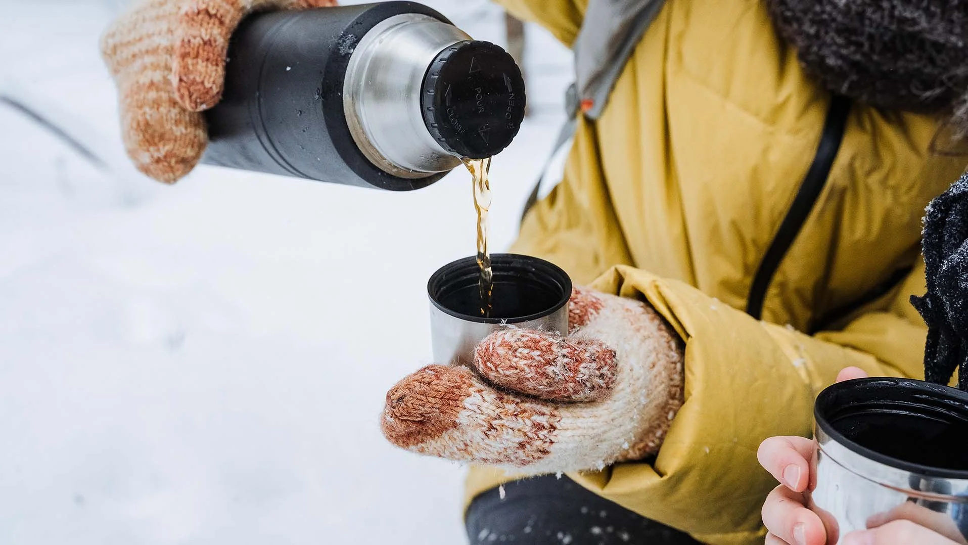 Close-up of hands in knit mittens holding thermos cup in snowy alpine setting, beverage lifestyle shoot on location at RAVN HAUS, Mt. Hood.